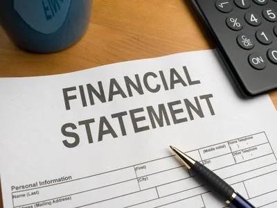 A financial statement form on a wooden desk with a pen, calculator, and a blue mug nearby.
