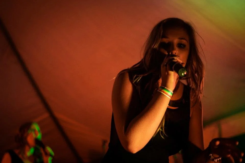 A young woman singing into a microphone on stage under colorful lighting.