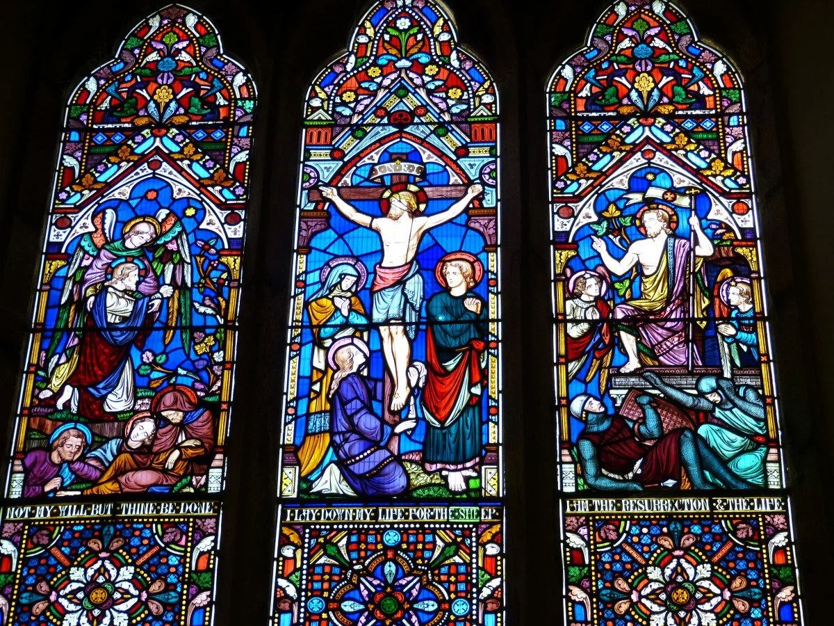 Colorful stained glass window depicting biblical scenes of Jesus' crucifixion, resurrection, and others, with intricate floral and geometric patterns.