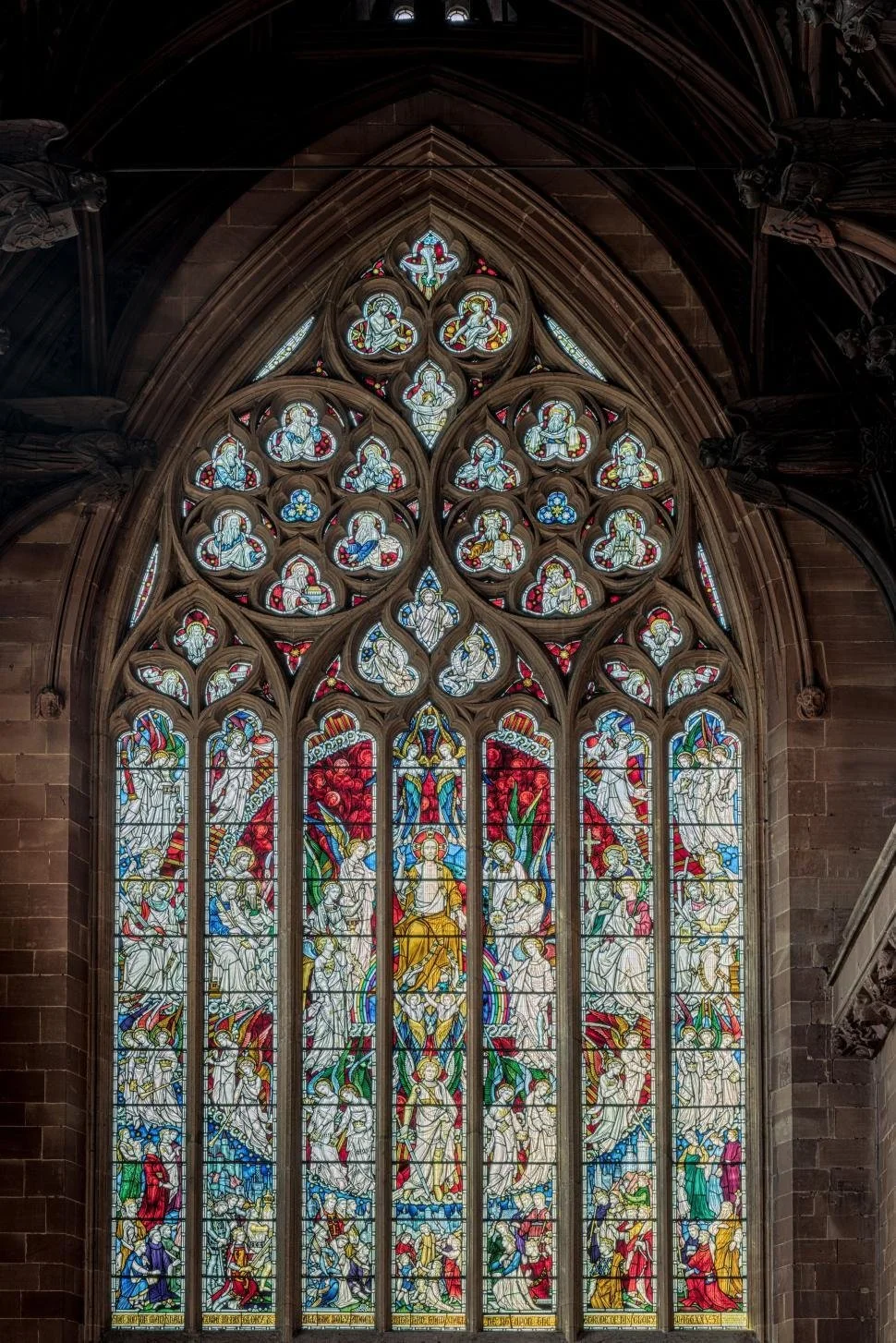 Colorful stained glass window in a cathedral or church with intricate designs depicting religious scenes and figures.