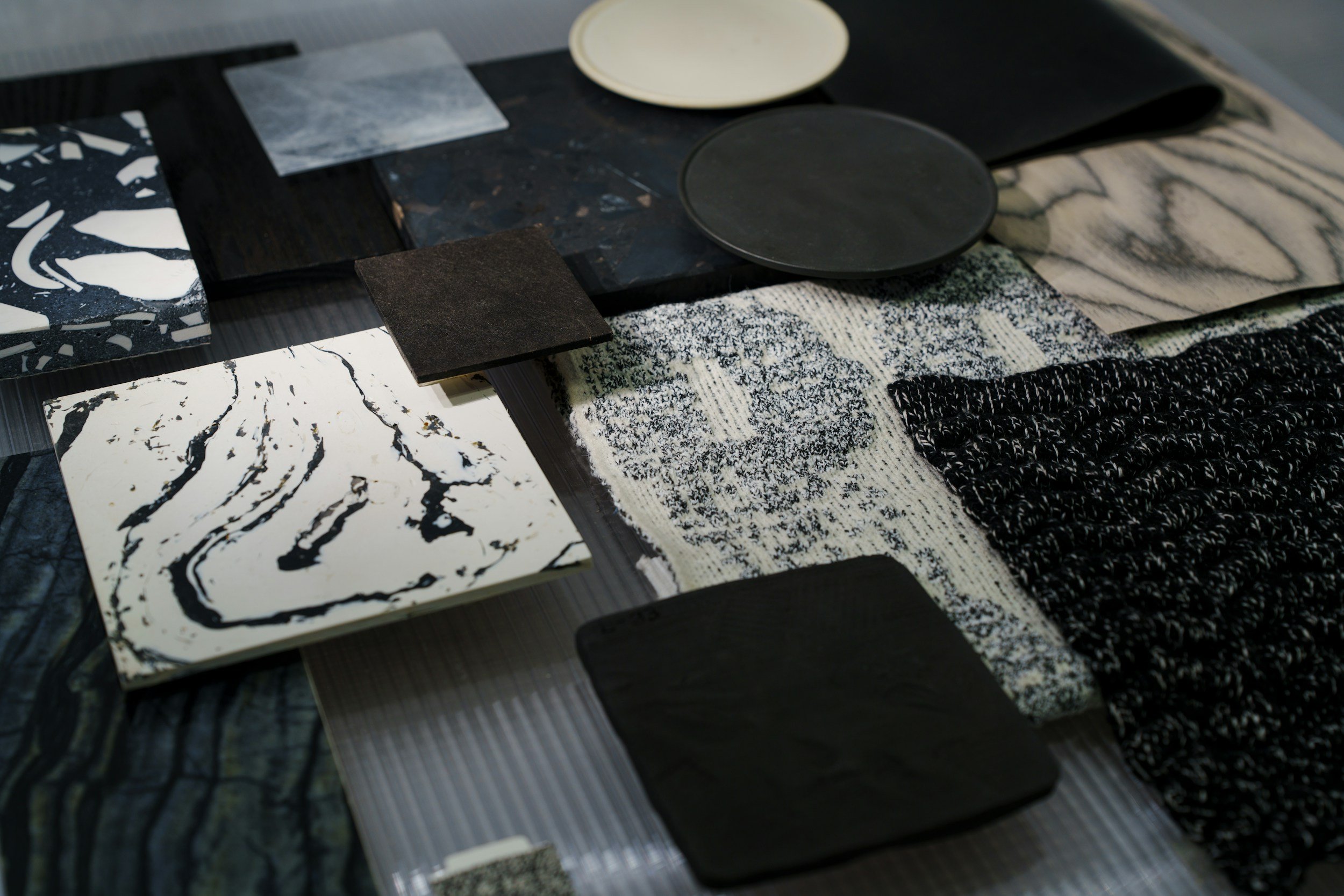 Collection of various patterned plates, tiles, and samples in black, white, gray, and beige tones, arranged on a table.