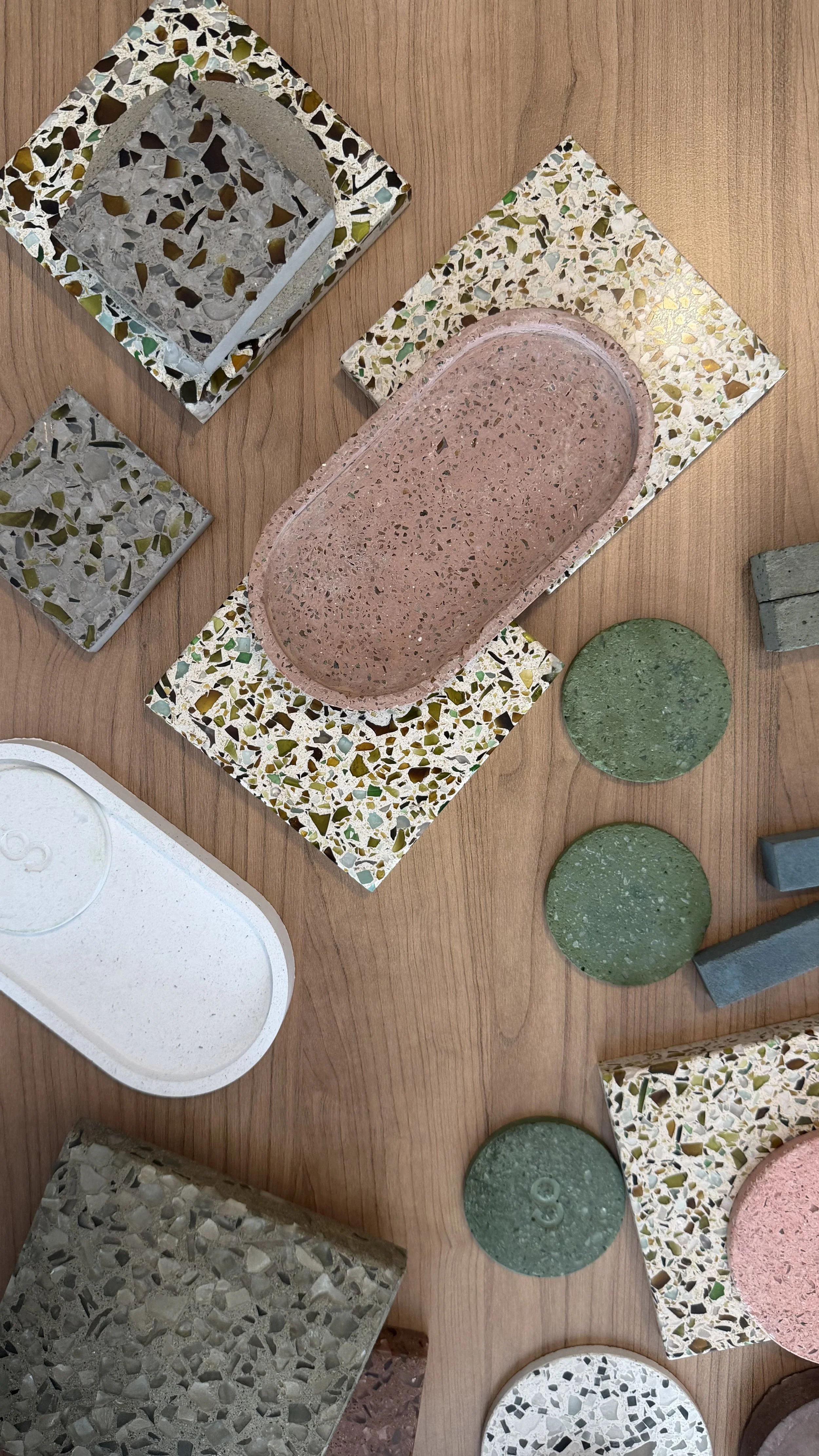 Various colorful terrazzo coasters, trays, and tiles on a wooden surface.