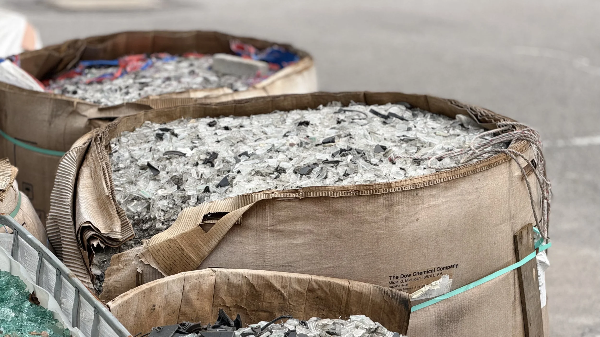 Bags filled with shredded glass and plastic materials at a recycling or waste collection site.