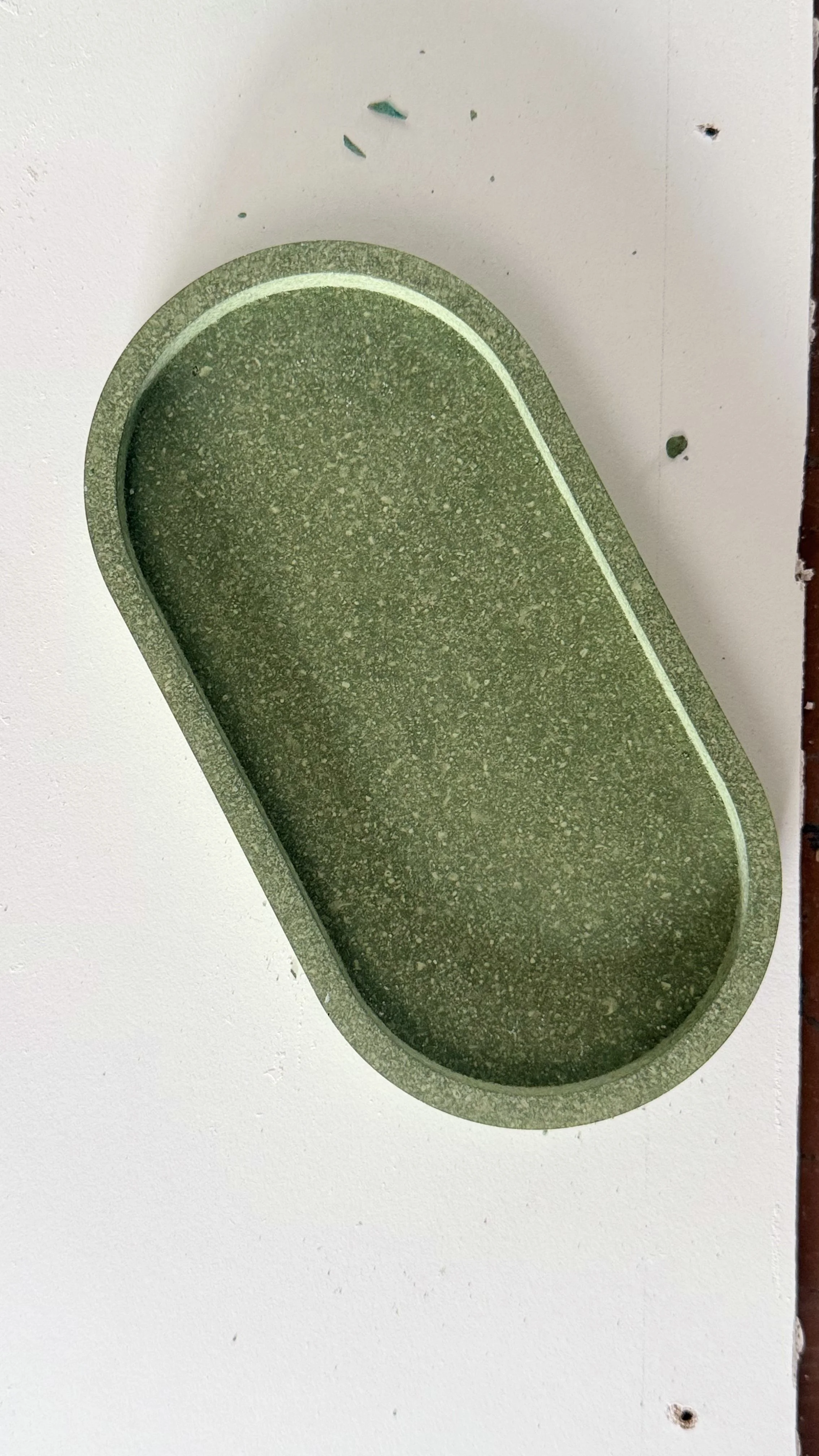 A green rectangular tray with rounded edges and a slightly textured surface, mounted on a white wall.