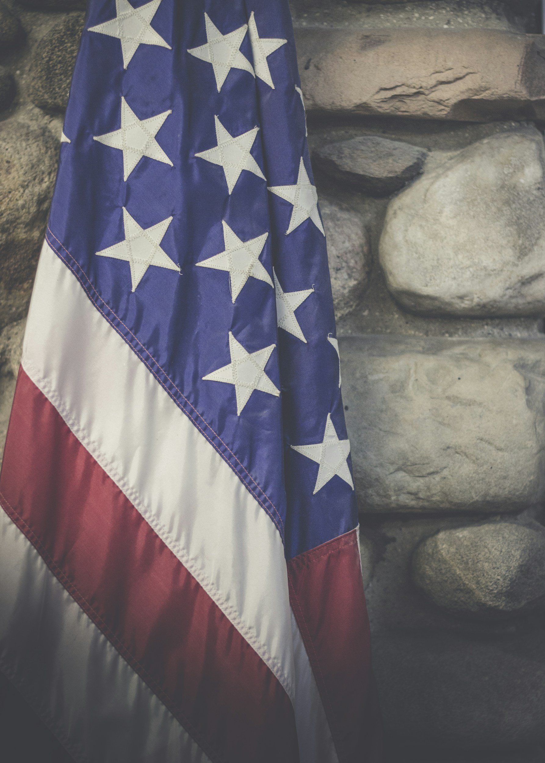 Close-up of a folded American flag with stars and stripes, hanging against a stone wall.