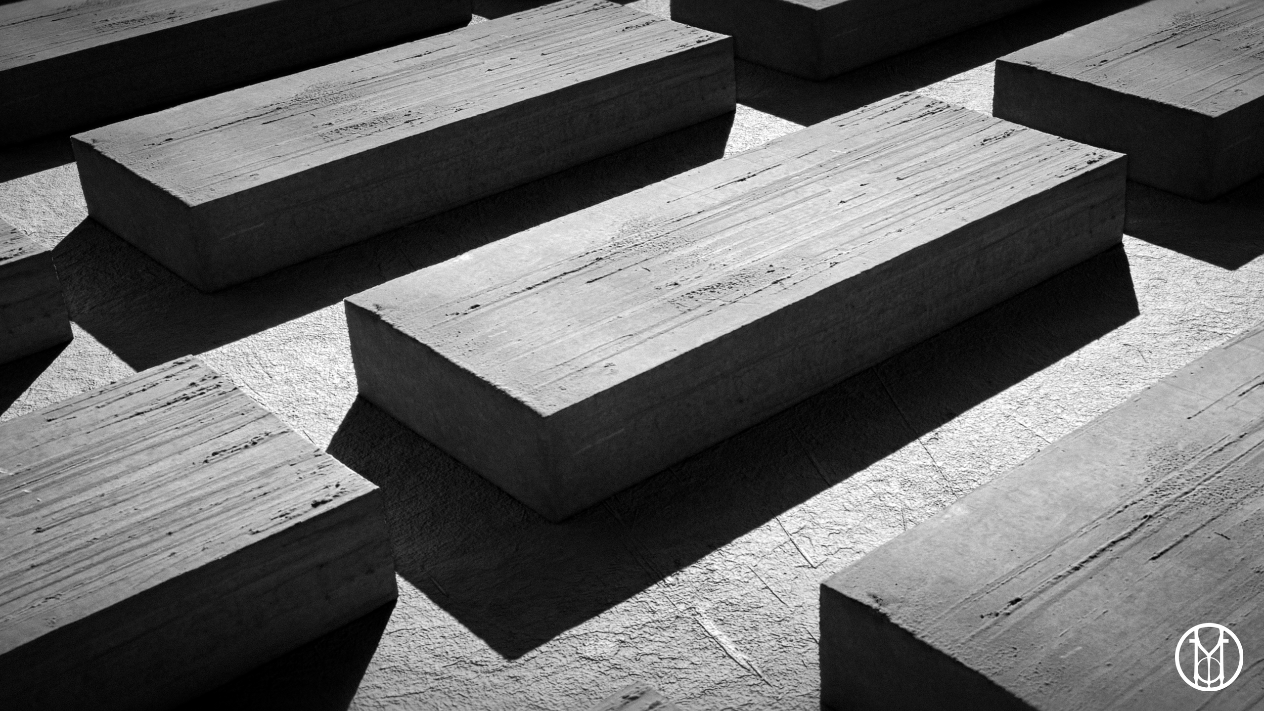 Multiple wooden planks arranged on a textured surface, casting shadows in a monochrome composition.