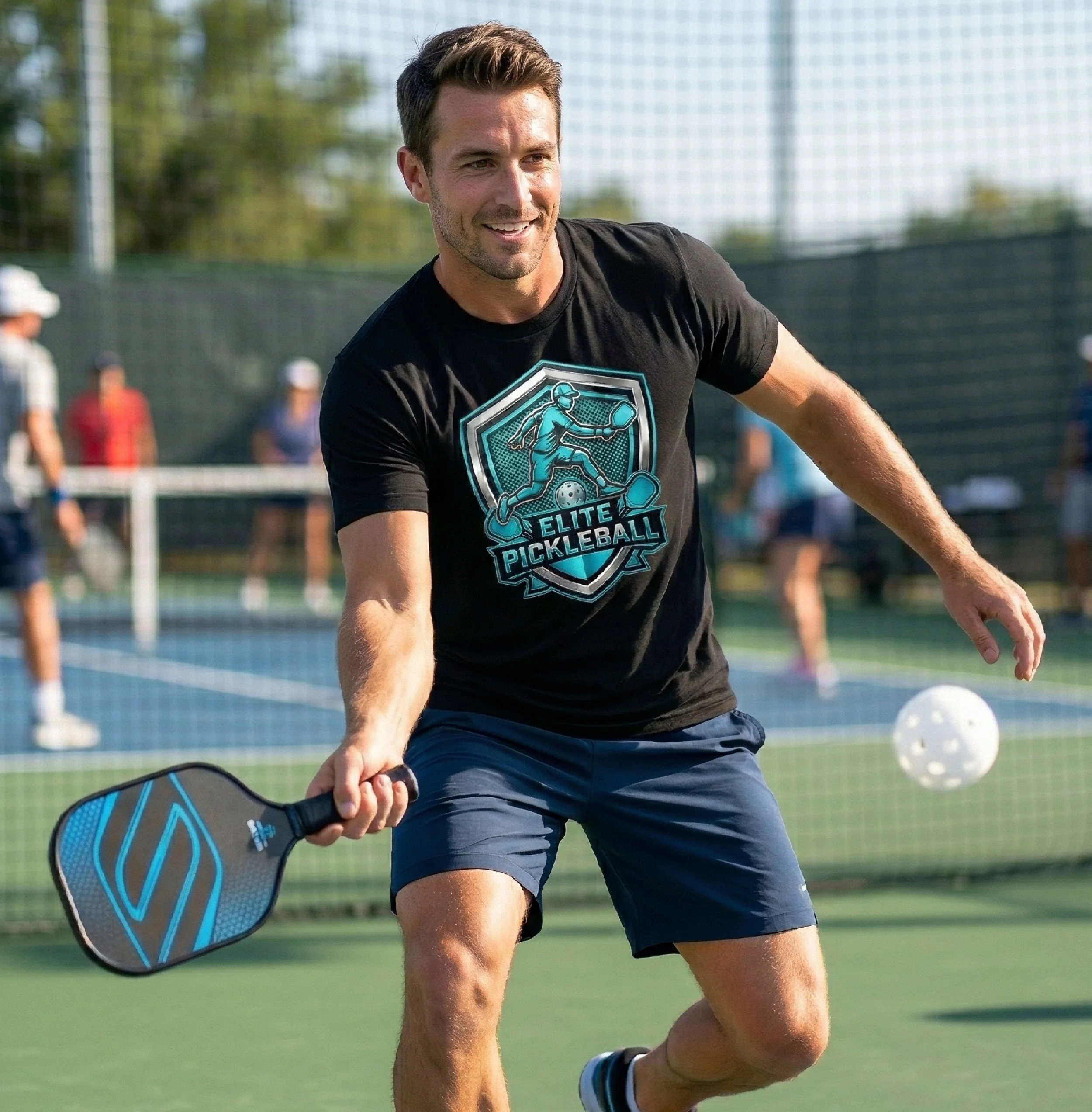 A man playing pickleball outdoors on a sunny day, holding a paddle, wearing a black t-shirt with a pickleball logo, and dark shorts.