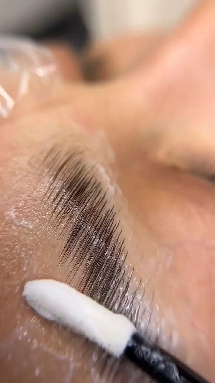 Close-up of a person's eyelashes being curled with a white eyelash curler, with skin visible in the background.