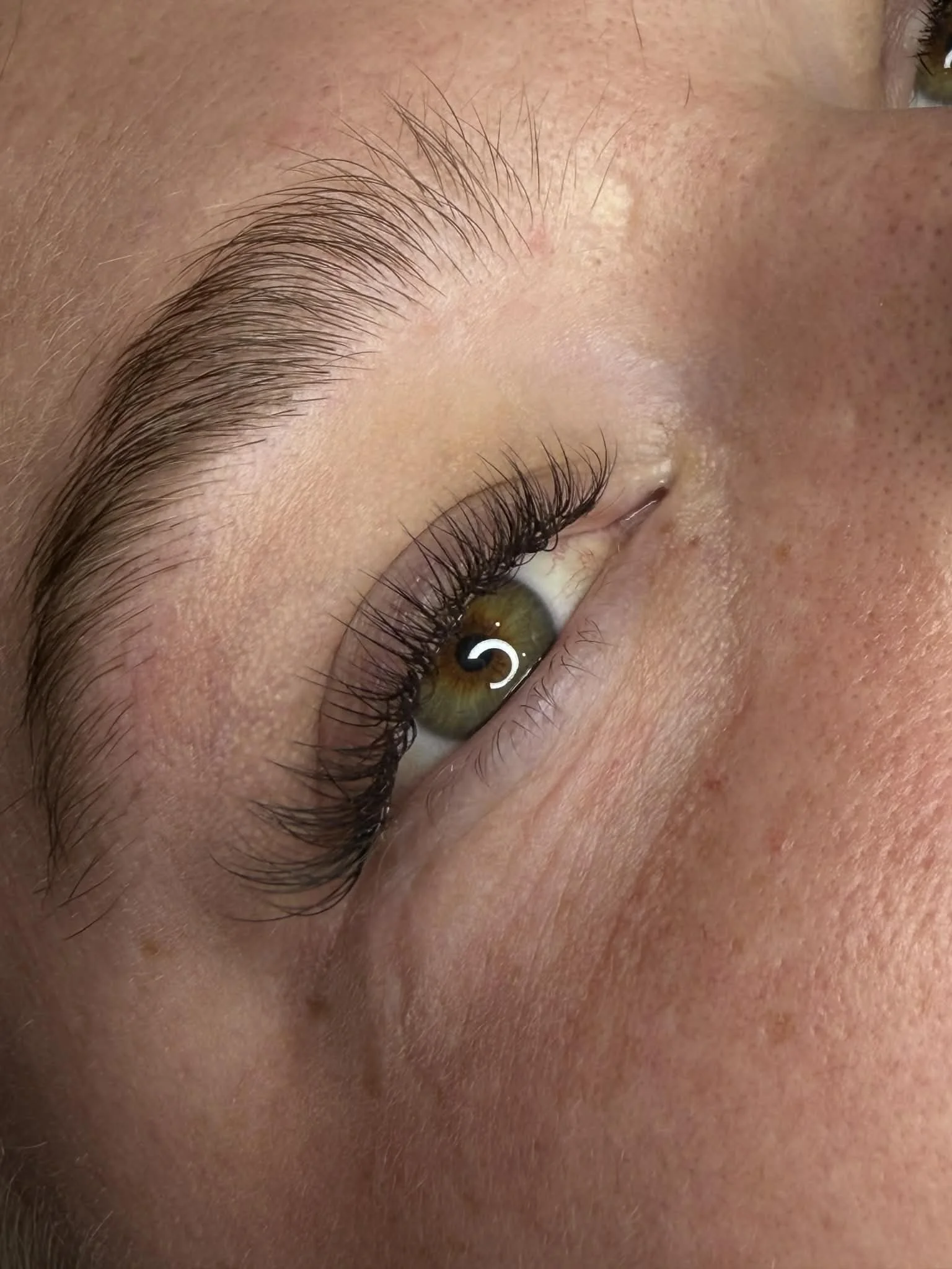 Close-up of a person's eye showing green iris, long eyelashes, and well-shaped eyebrows.
