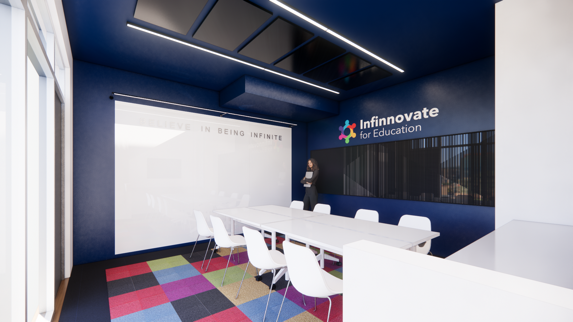 Modern conference room with a long white table, white chairs, dark blue walls, a whiteboard, and the logo 'Innotvate for Education' on the wall. A woman stands near the wall, and the room has a colorful carpet.