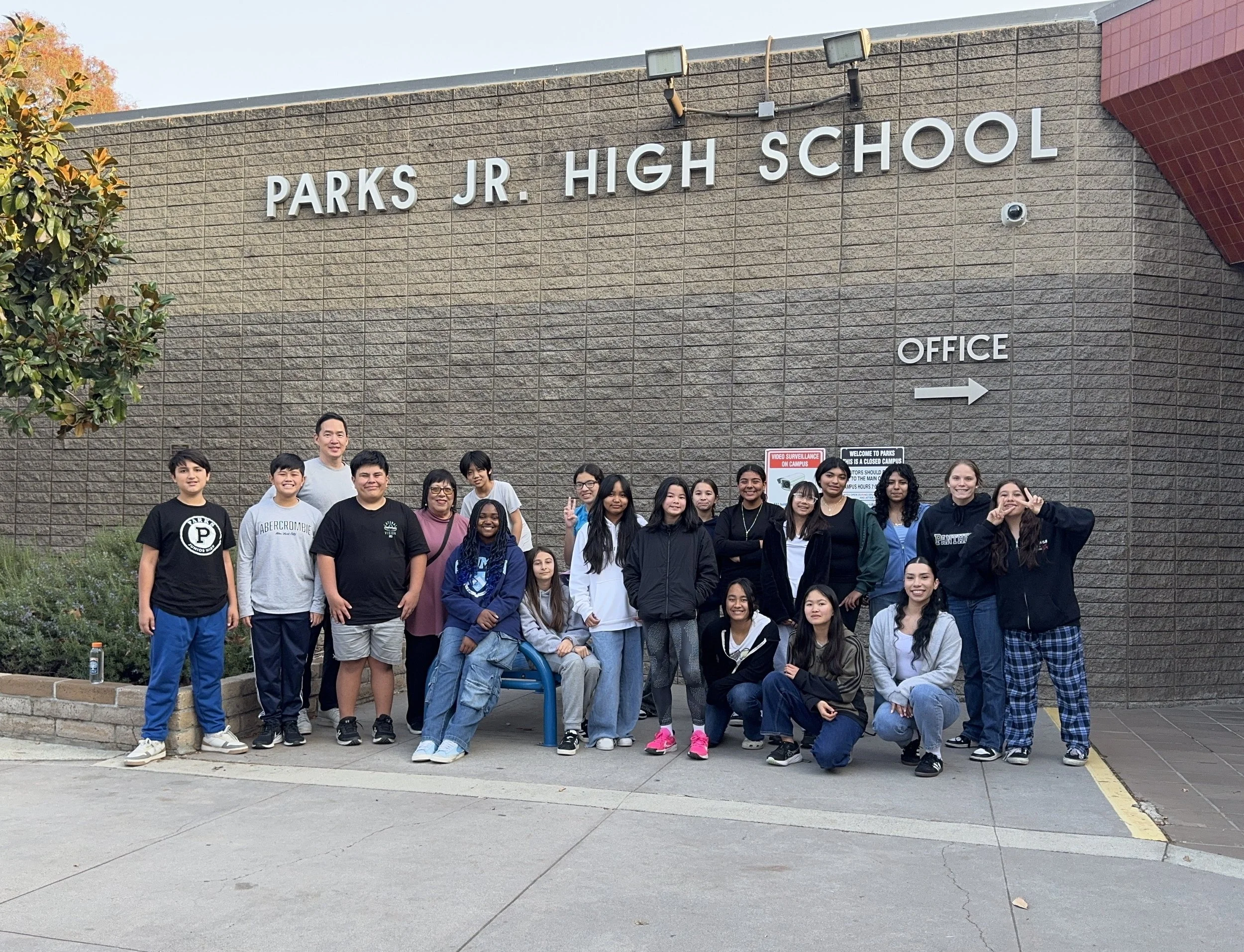 A group of students and two adults standing in front of Parks Jr. High School building, smiling and posing for the photo.