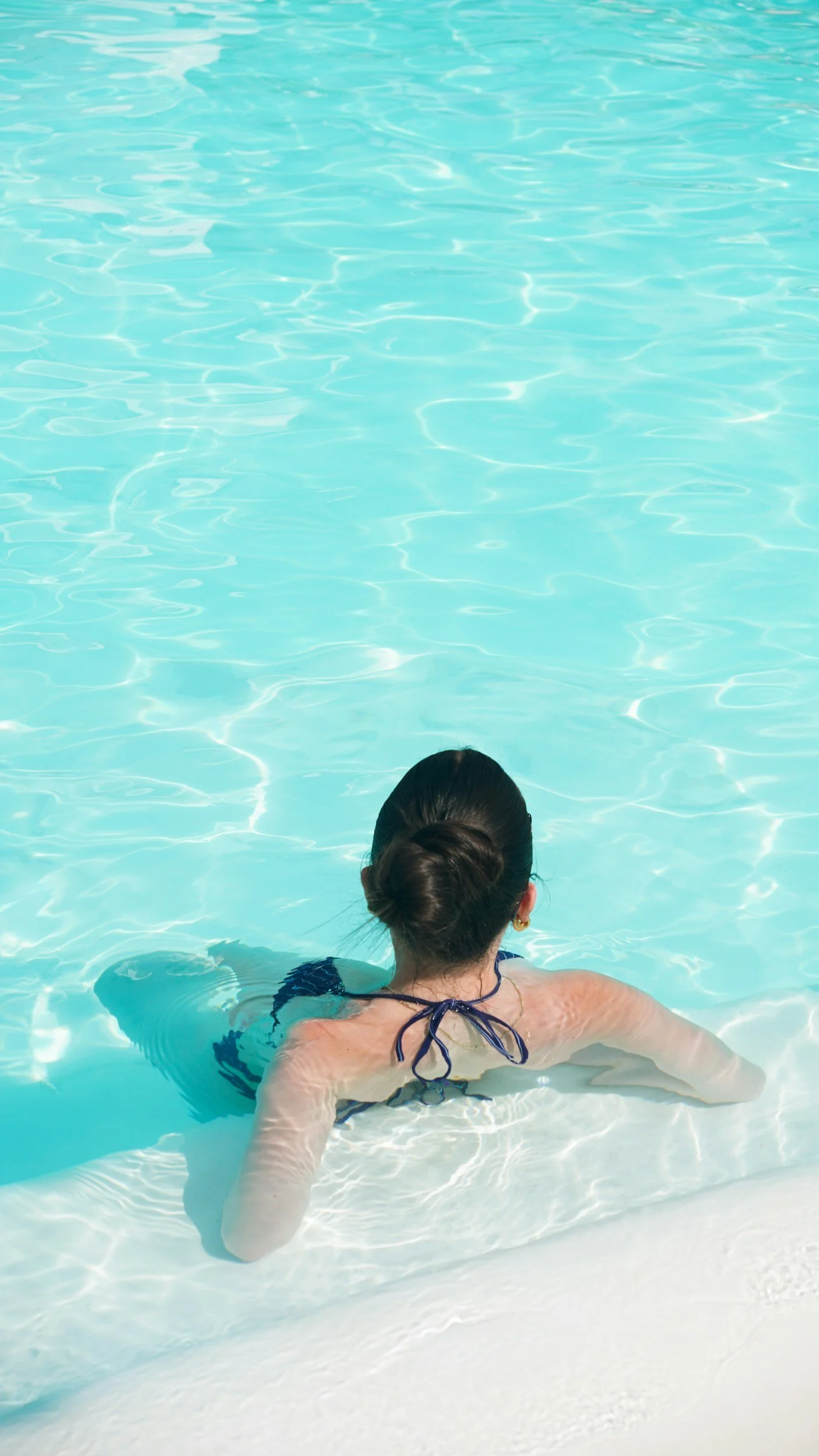 A woman with dark hair in a bun swimming in a pool, viewed from behind.
