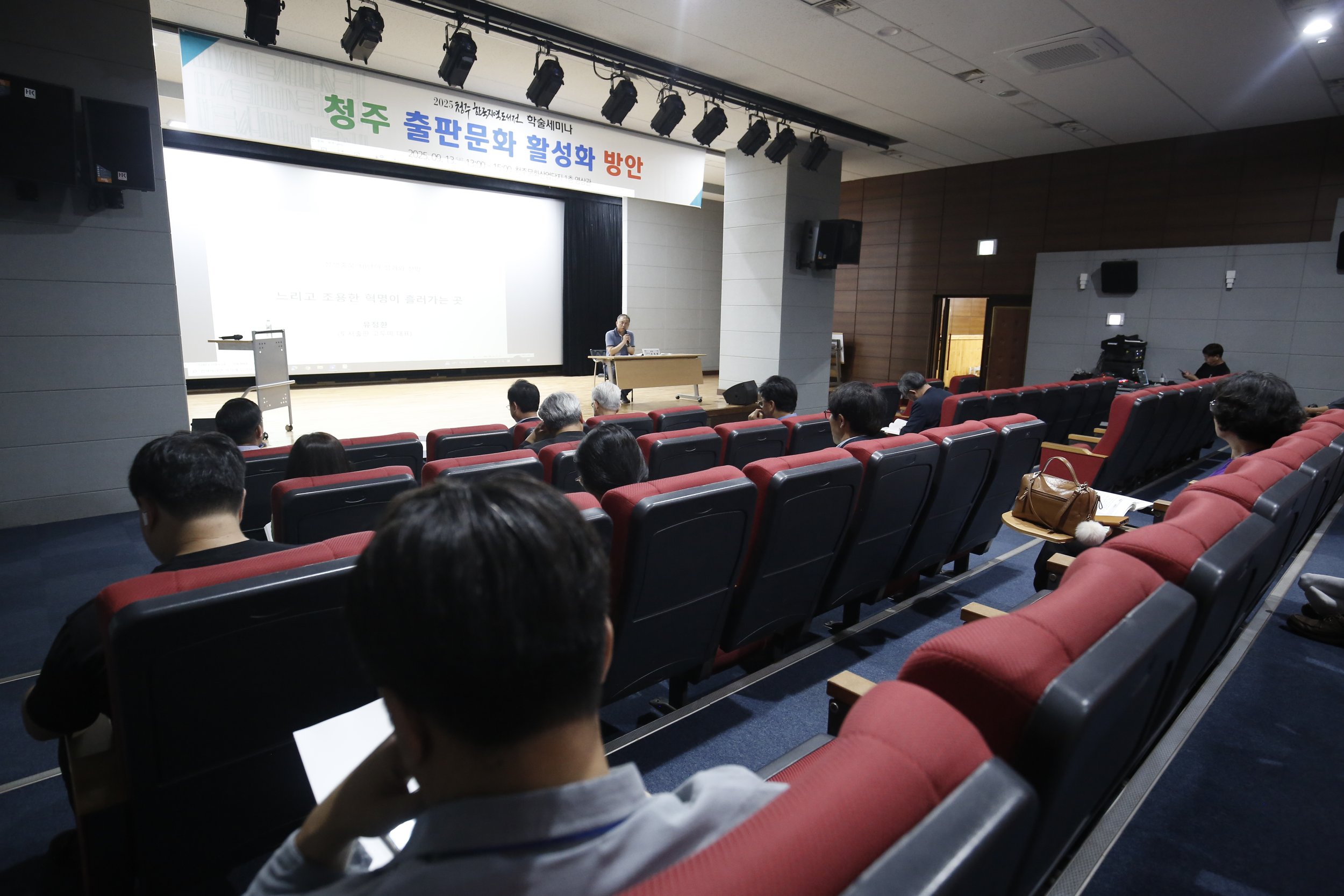 청주 출판문화 활성화 방안 학술세미나가 개최되는 강당 내부 모습. 청중들이 앉아 있고 강연자가 무대에서 발표 중임.