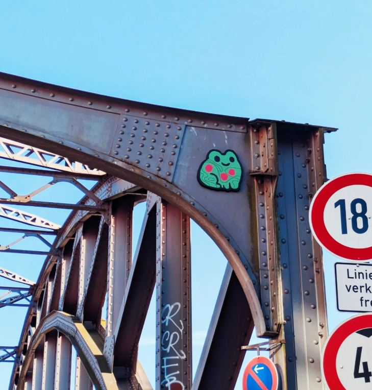 Close-up of an old metal bridge with a frog sticker on the arch and traffic signs nearby.