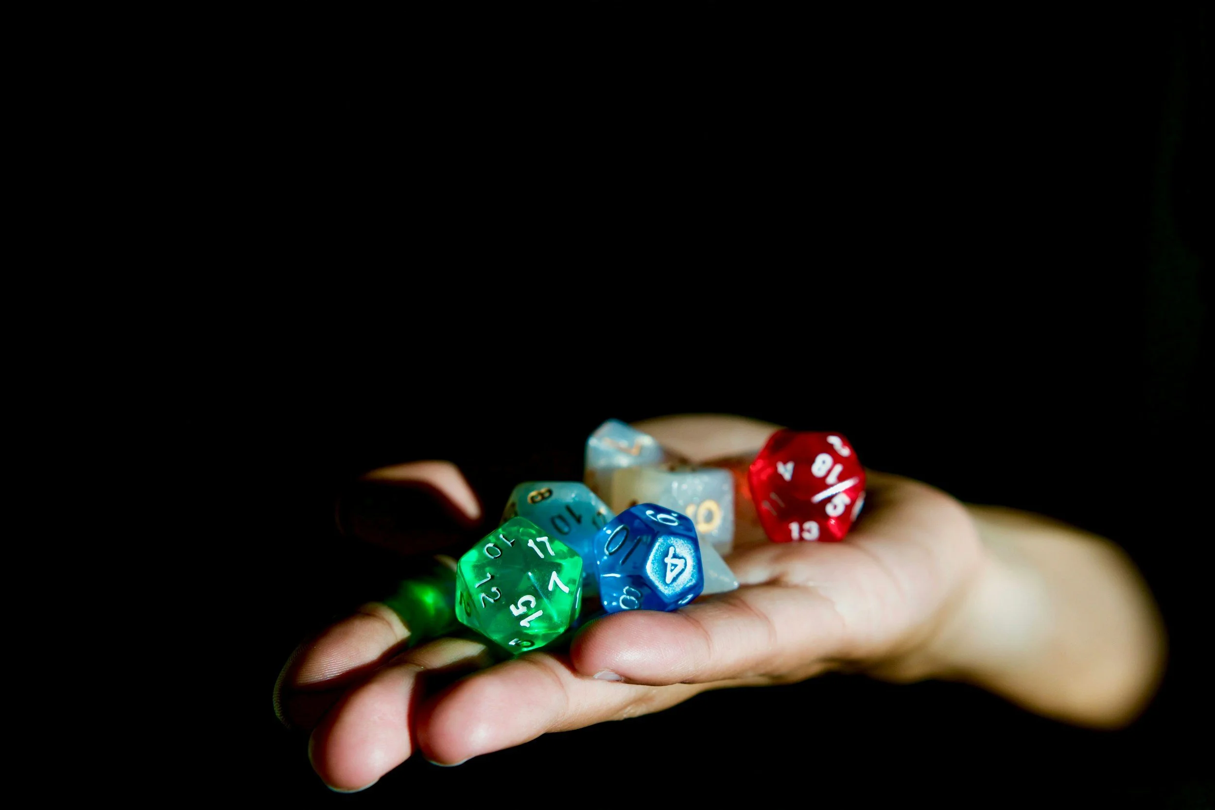 Eine Hand hält mehrere bunte, sechseckige Würfel mit Zahlen, die für Würfelspiele wie D&D oder Rollenspiele verwendet werden, vor einem schwarzen Hintergrund.