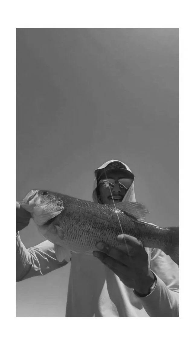 Person wearing sunglasses, a cap, and a hoodie holding a large fish against a clear sky.
