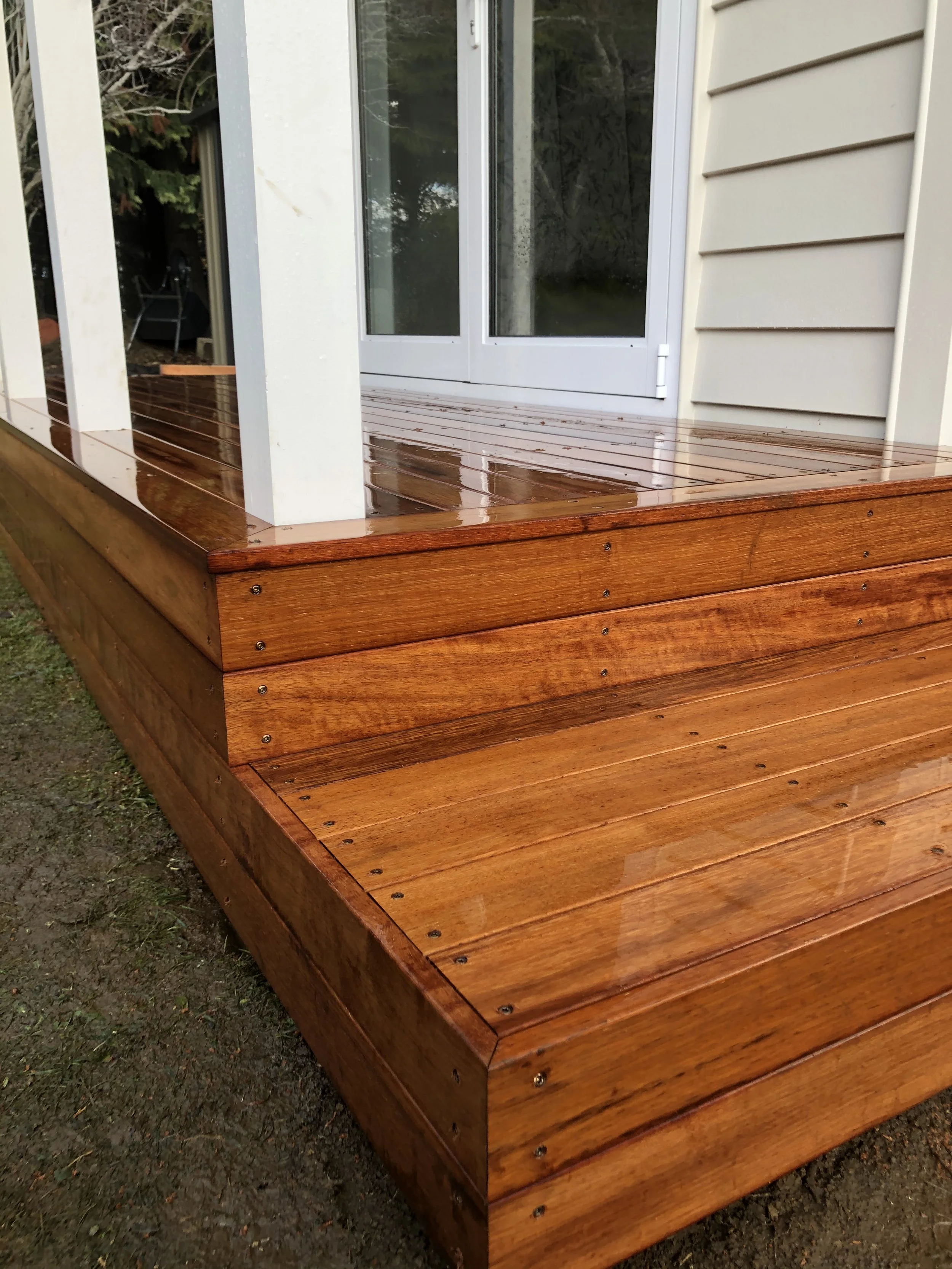 Wooden deck in front of sliding glass door, with a white corner post, on grassy terrain.