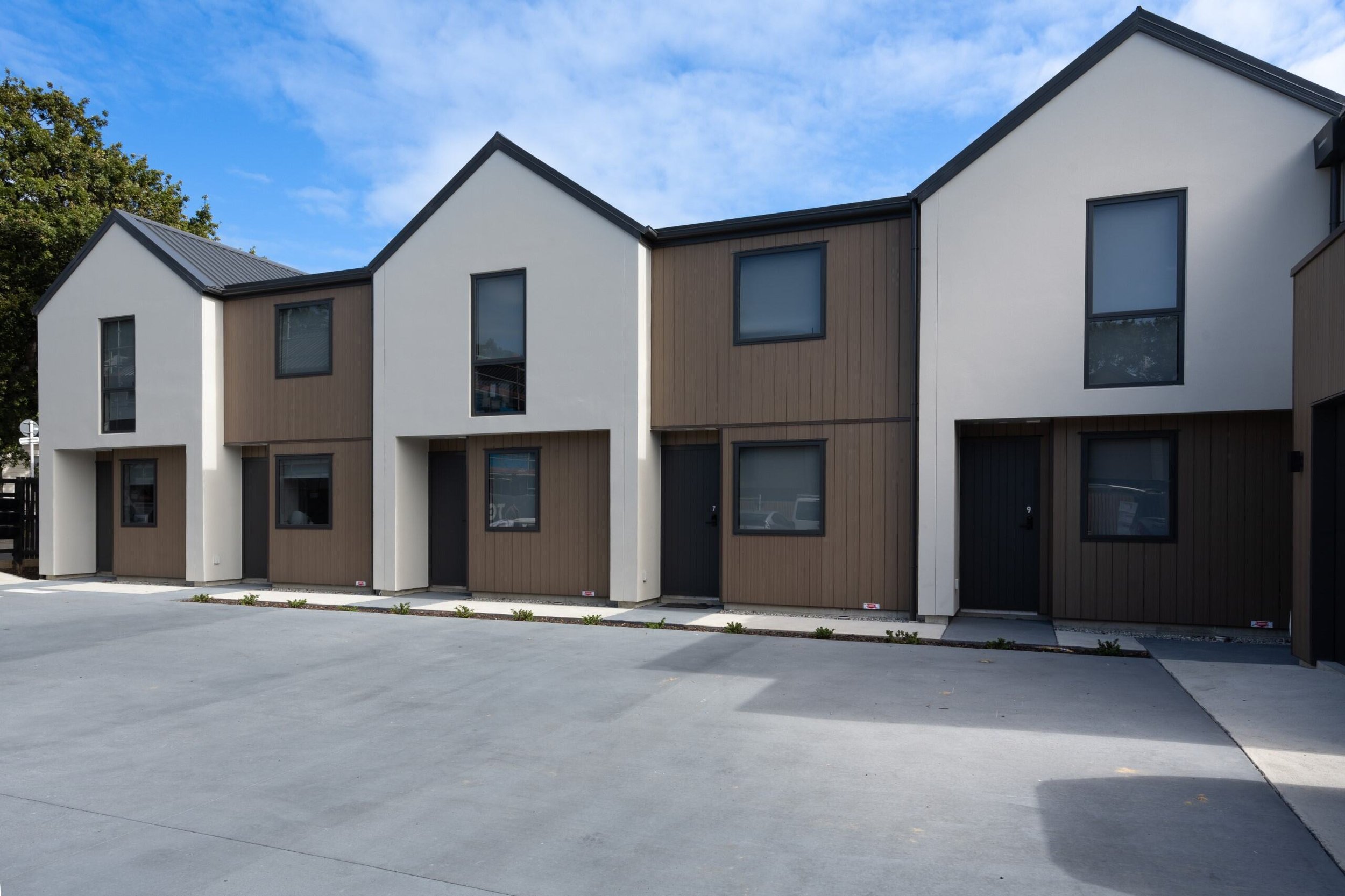 Modern townhouse complex with alternating white and wood-paneled facades under a blue sky.