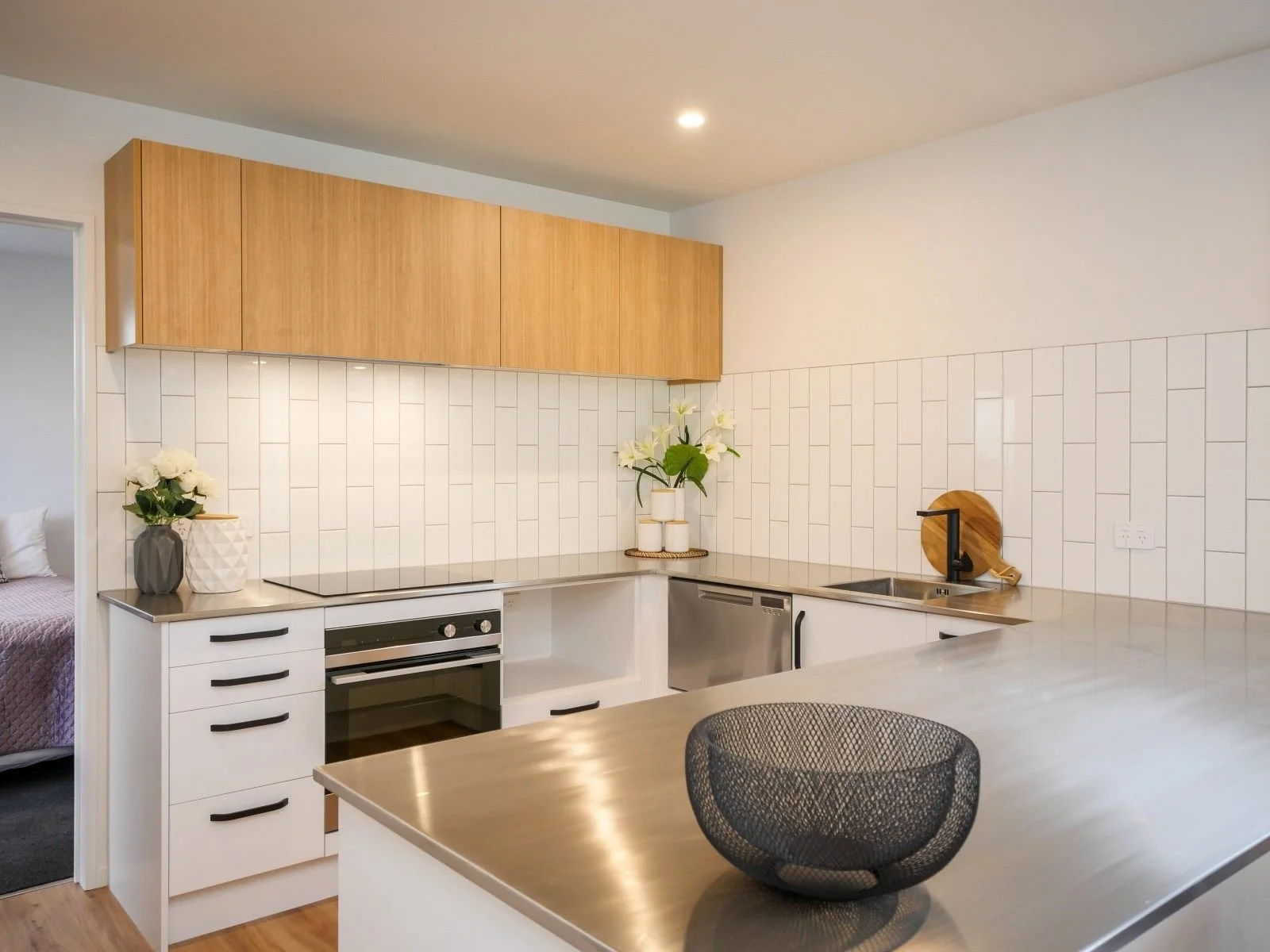 Modern kitchen with white and wood cabinets, white tiled backsplash, stainless steel appliances, and decorative flowers on the counter.