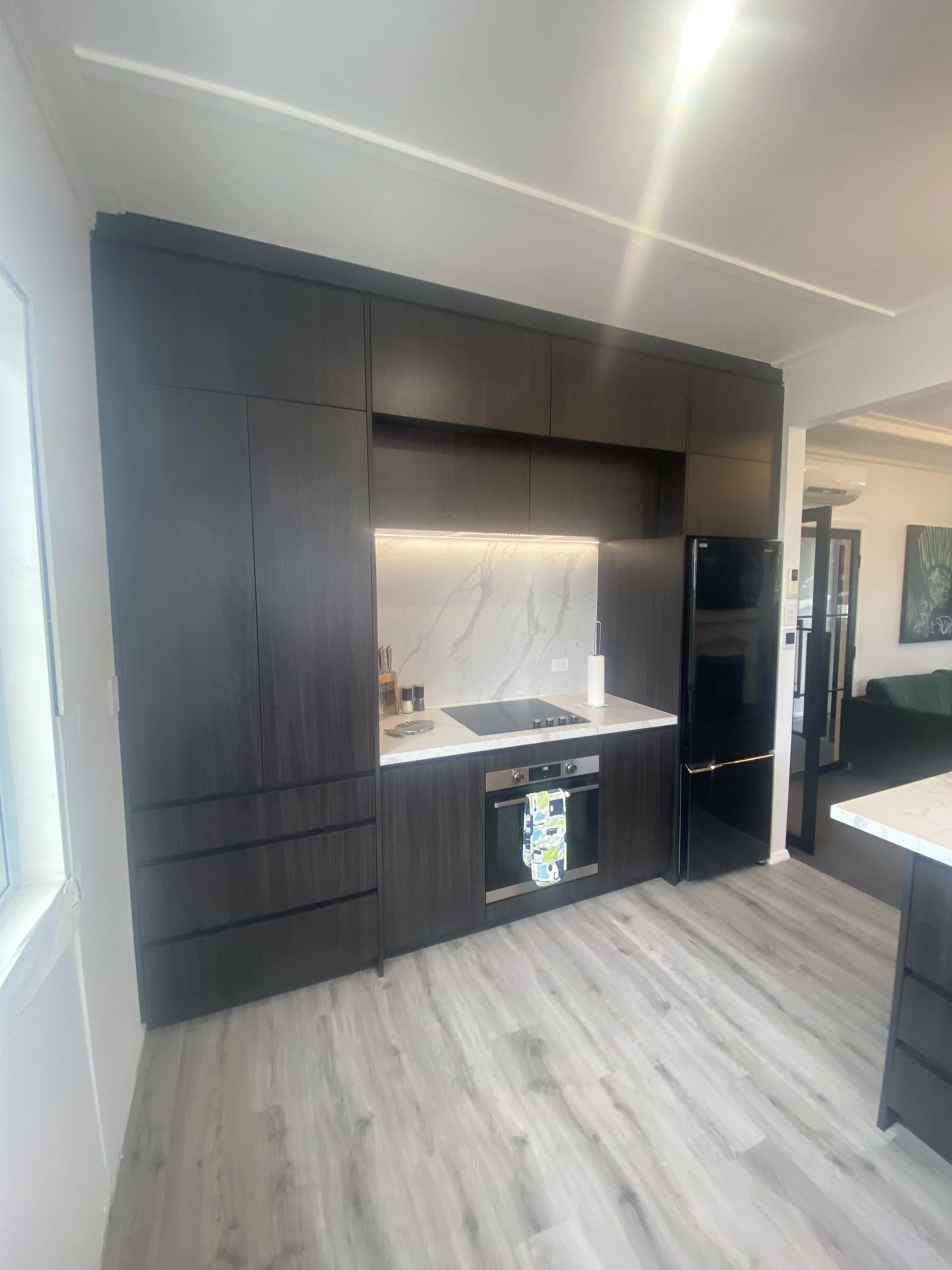 Modern kitchen with dark wood cabinets, marble backsplash, and built-in oven, with light wood flooring.