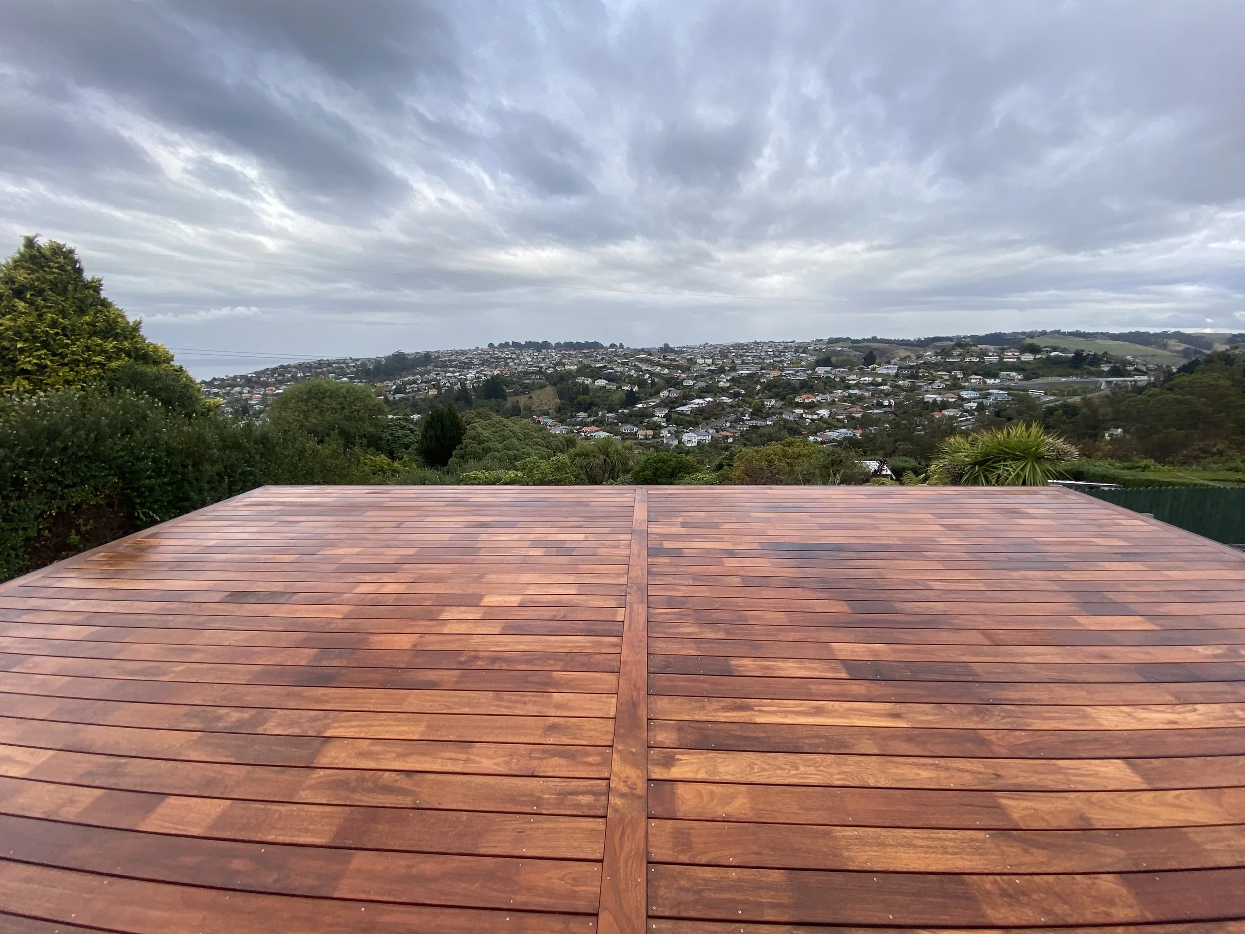 View from a wooden deck over a hillside town with houses, greenery, and cloudy sky.