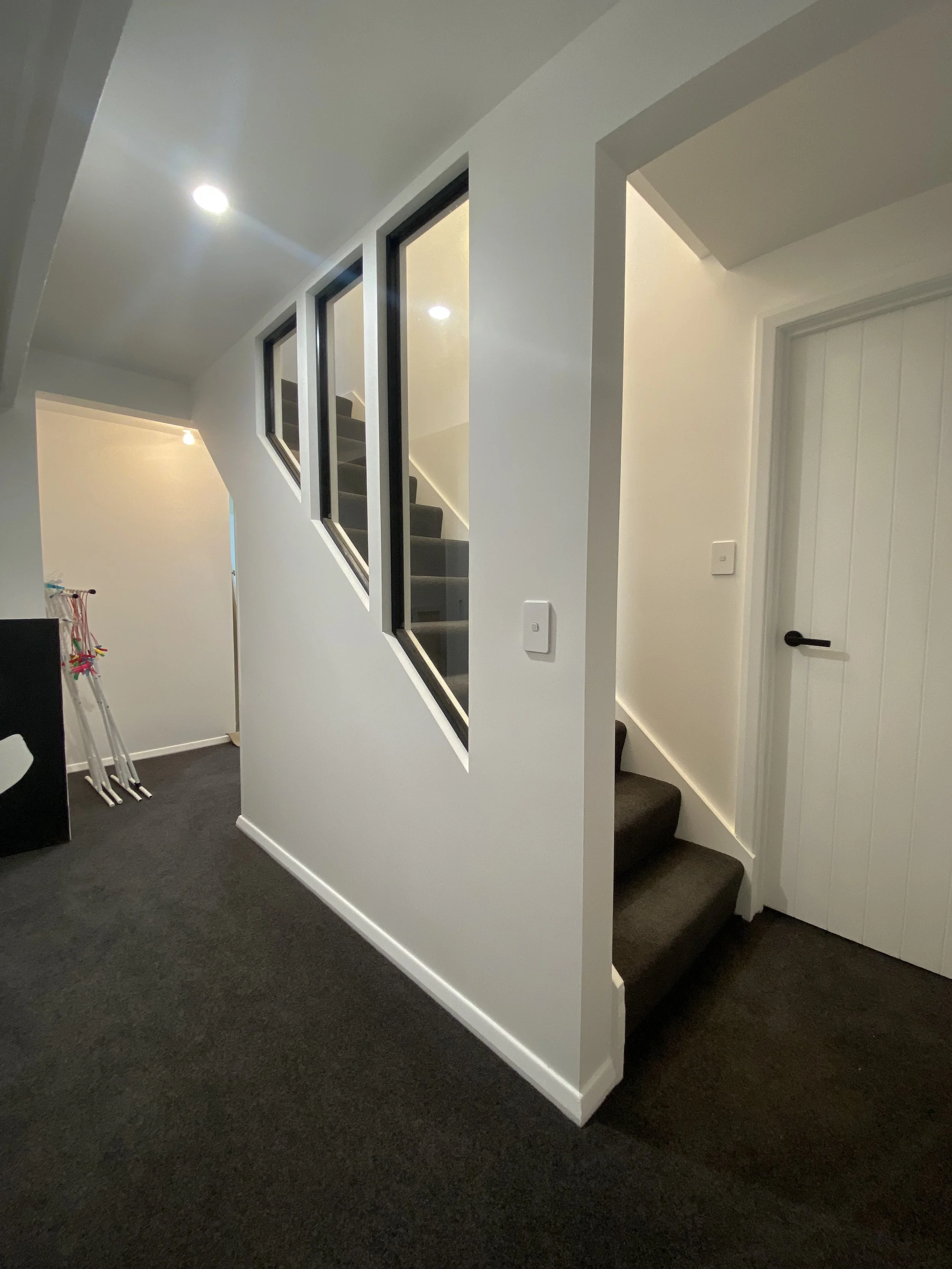 Interior view of a residential space with stairs, a door, and a partial wall with windows.