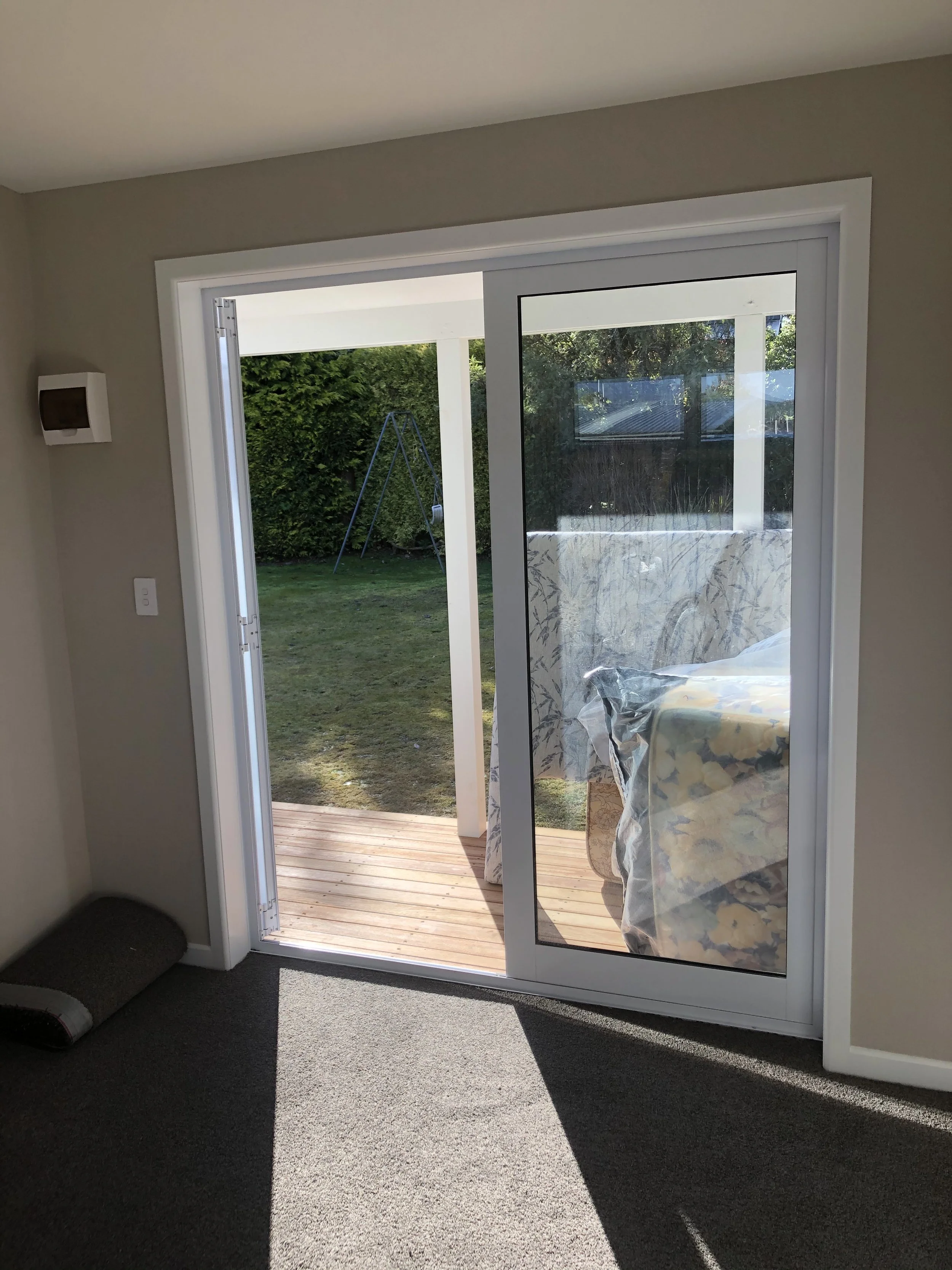 Sliding glass door leading to a grassy backyard with a wooden deck and a metal swing set.