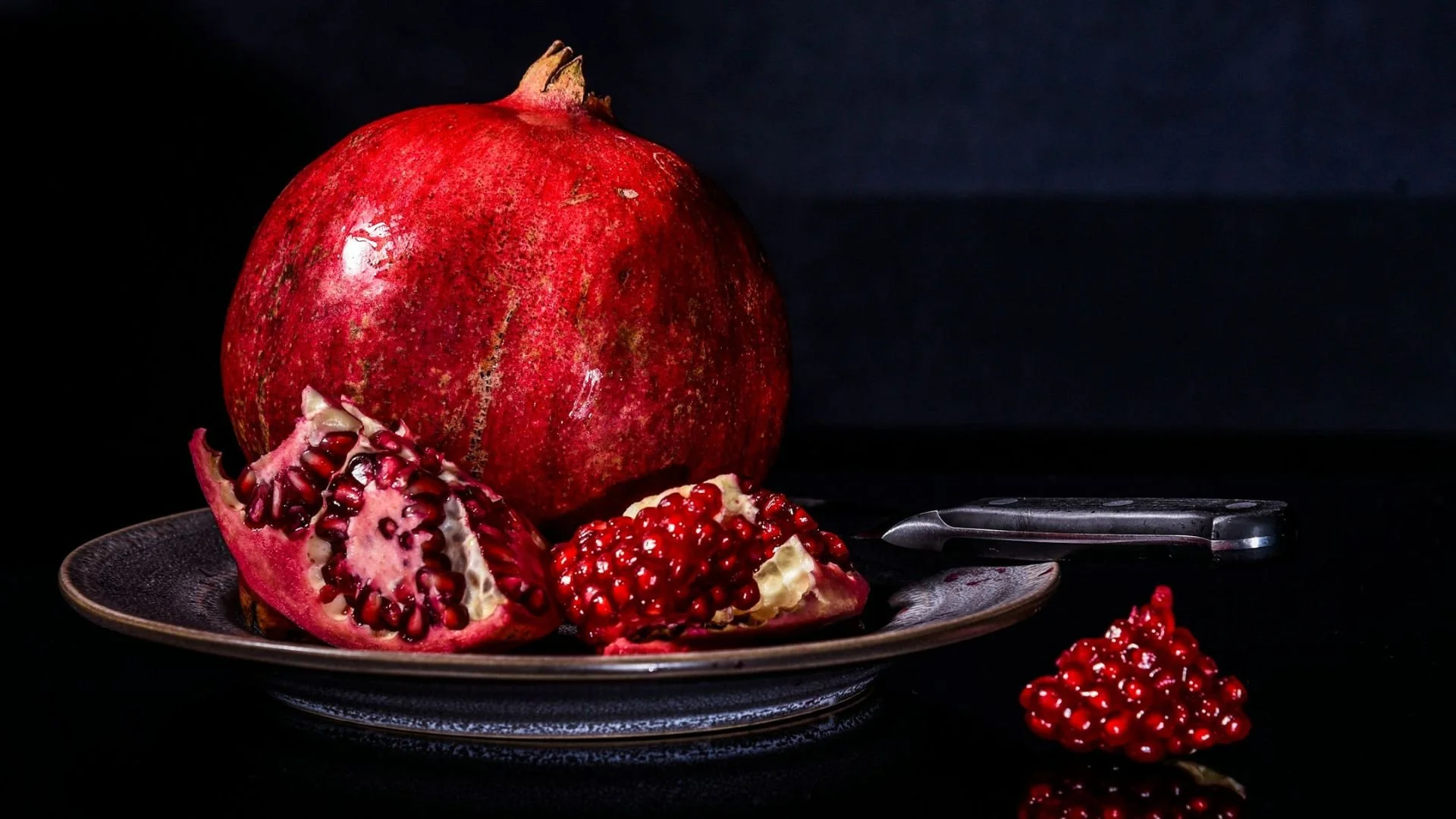 A whole pomegranate on a dish with fragments of other pomegranate