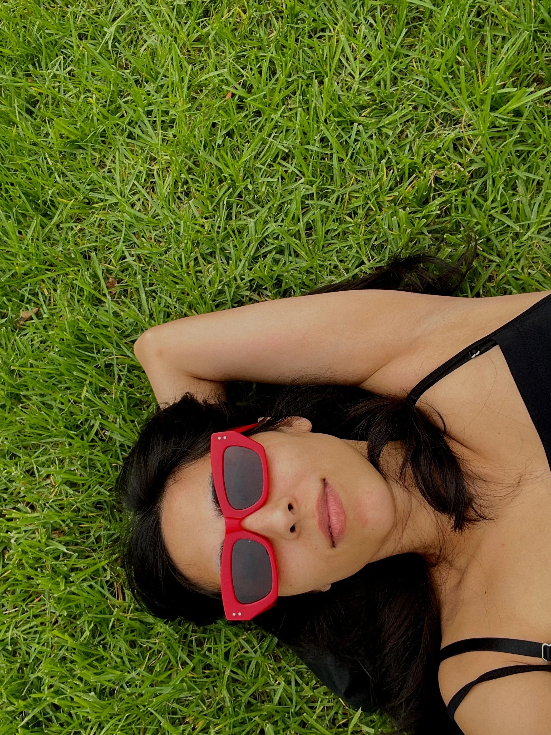 An aerial photograph of Newtown astrologer Rebecca Mitchell laying in the grass wearing red sunglasses