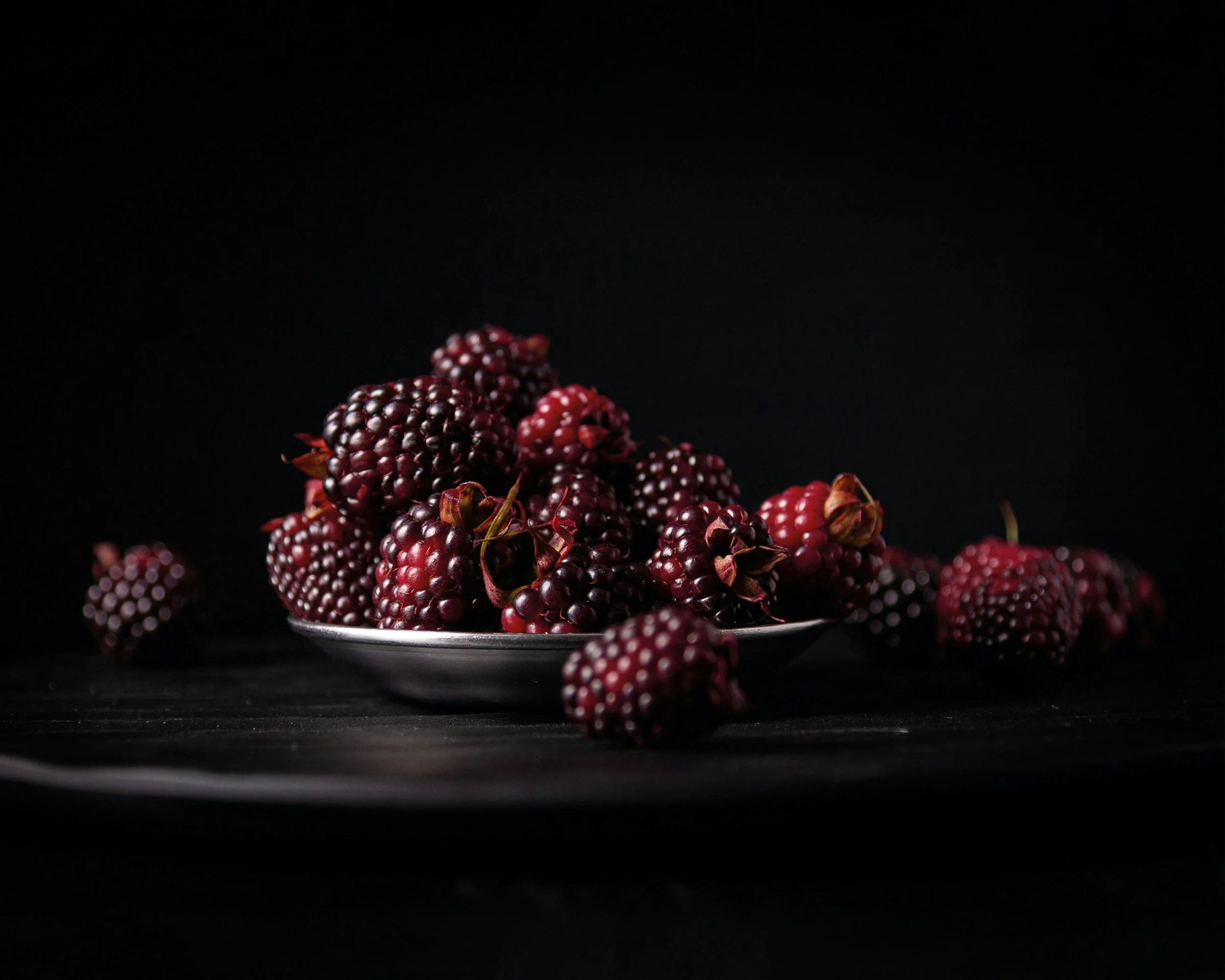 a small metal silver dish overflowing with with deep red raspberries