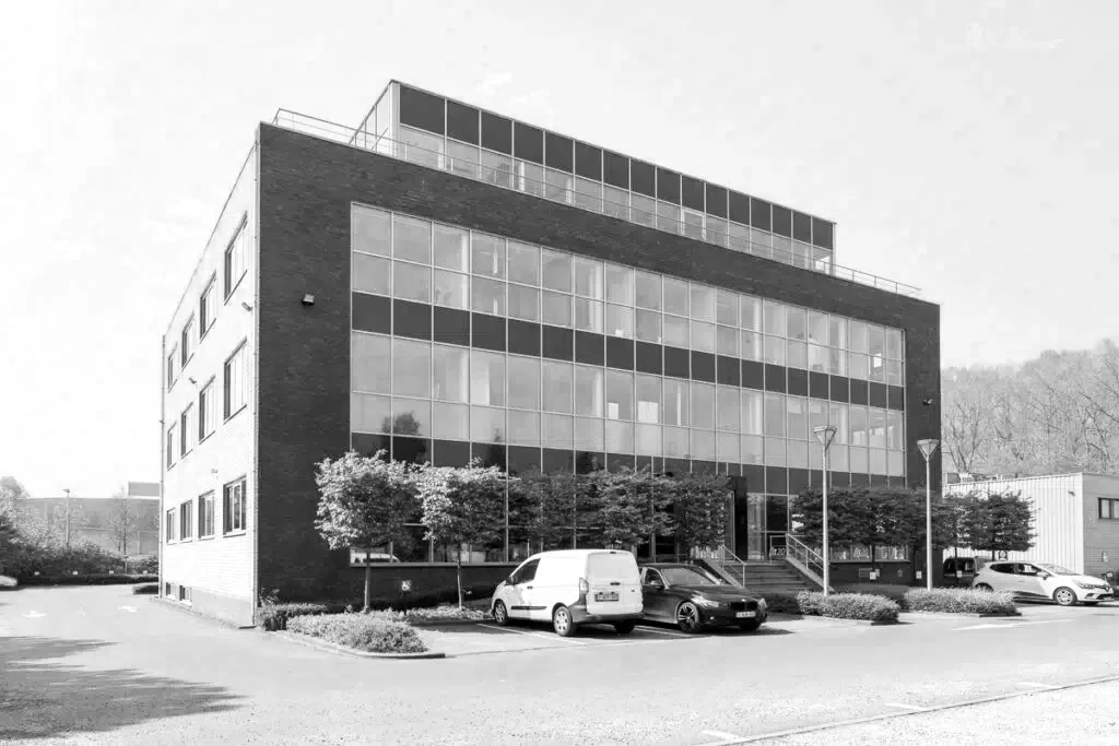 Modern office building with large glass windows, surrounded by parked cars and small trees.