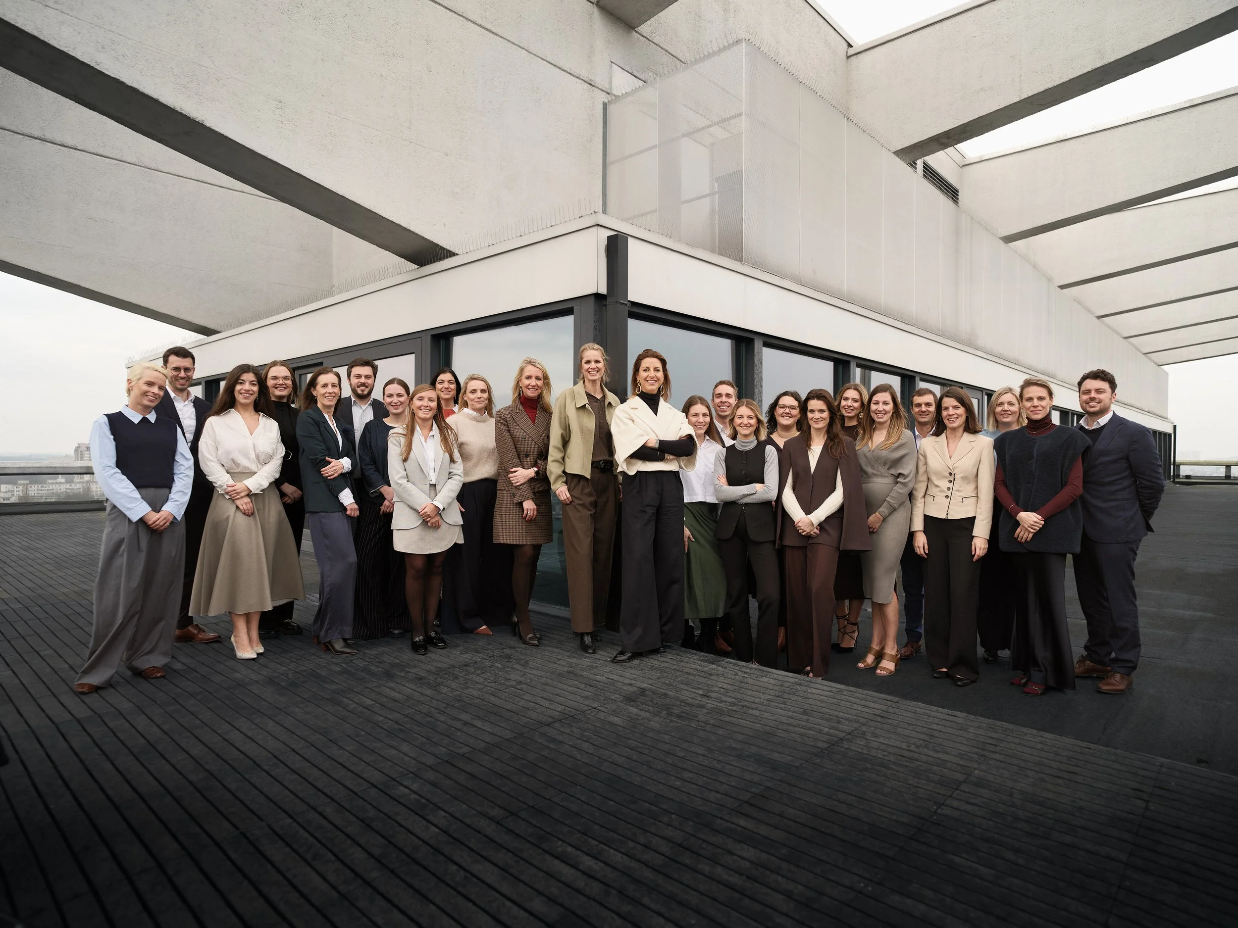 Group of people dressed in business casual attire standing on a rooftop with modern architecture in the background.