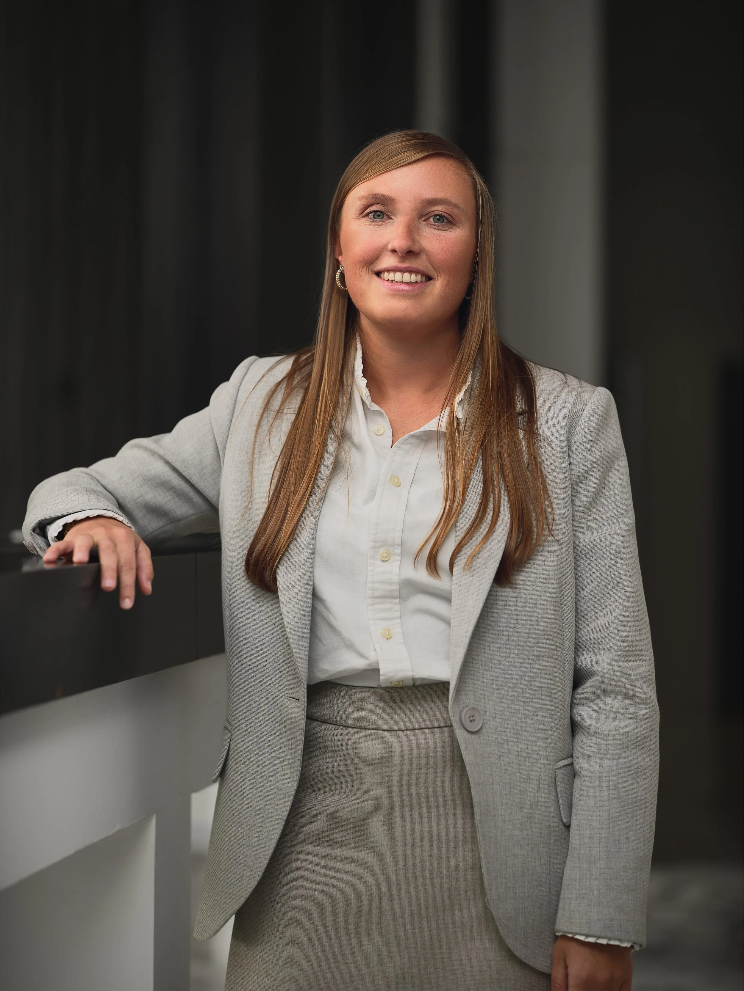A woman in a gray suit and white blouse smiling in a professional setting.