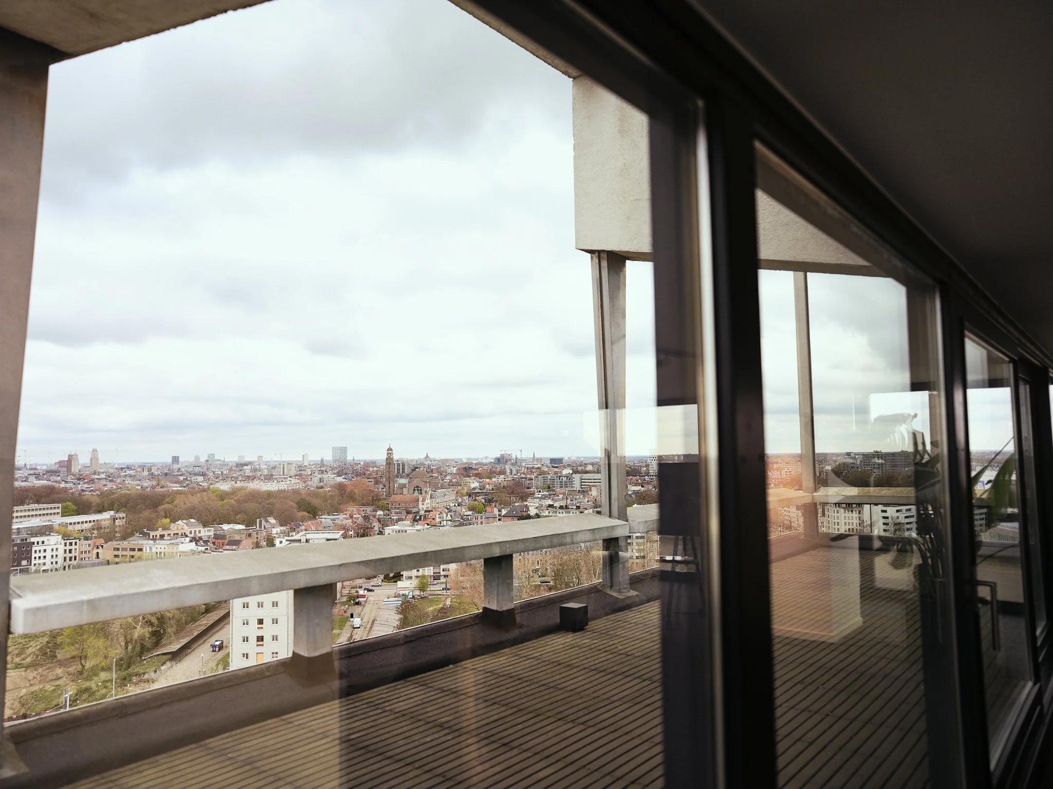 View of a city skyline through a large glass window from a high-rise balcony or apartment.