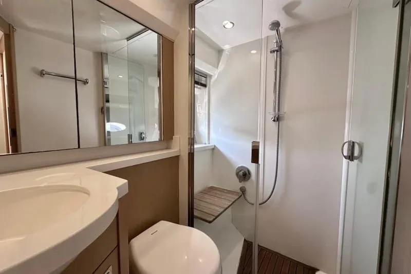 Small bathroom with a vanity sink, toilet, and a walk-in shower with glass door, showerhead, and wooden bench.
