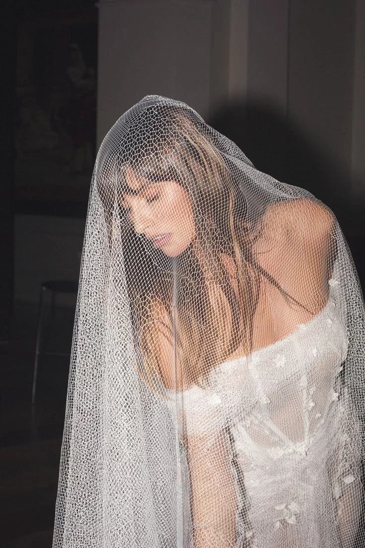 A woman wearing a wedding dress and veil, looking down with her mouth slightly open.