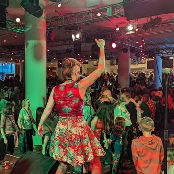 A woman wearing a red floral dress dancing at a crowded event with colorful lighting and people in the background.