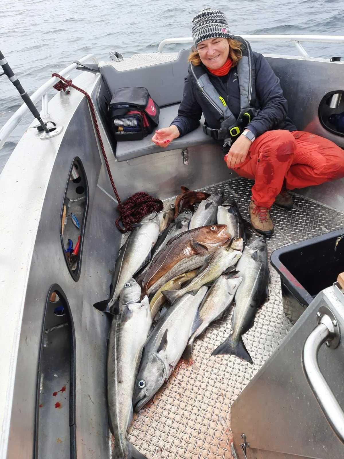 Eine Frau in einer Jolle mit gefangenen Fischen, lachend, bei einem Angelausflug auf dem Wasser.