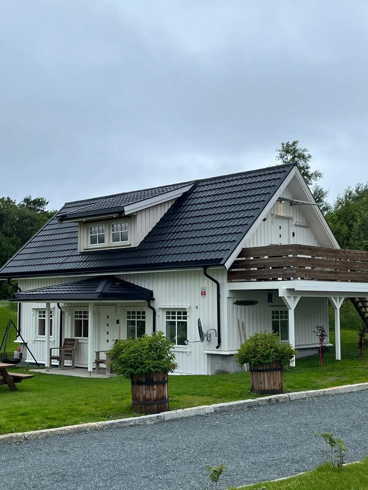 Ein weißes, zweistöckiges Haus mit schwarzen Dachziegeln, Terrassen, und umliegender grüner Rasenfläche.