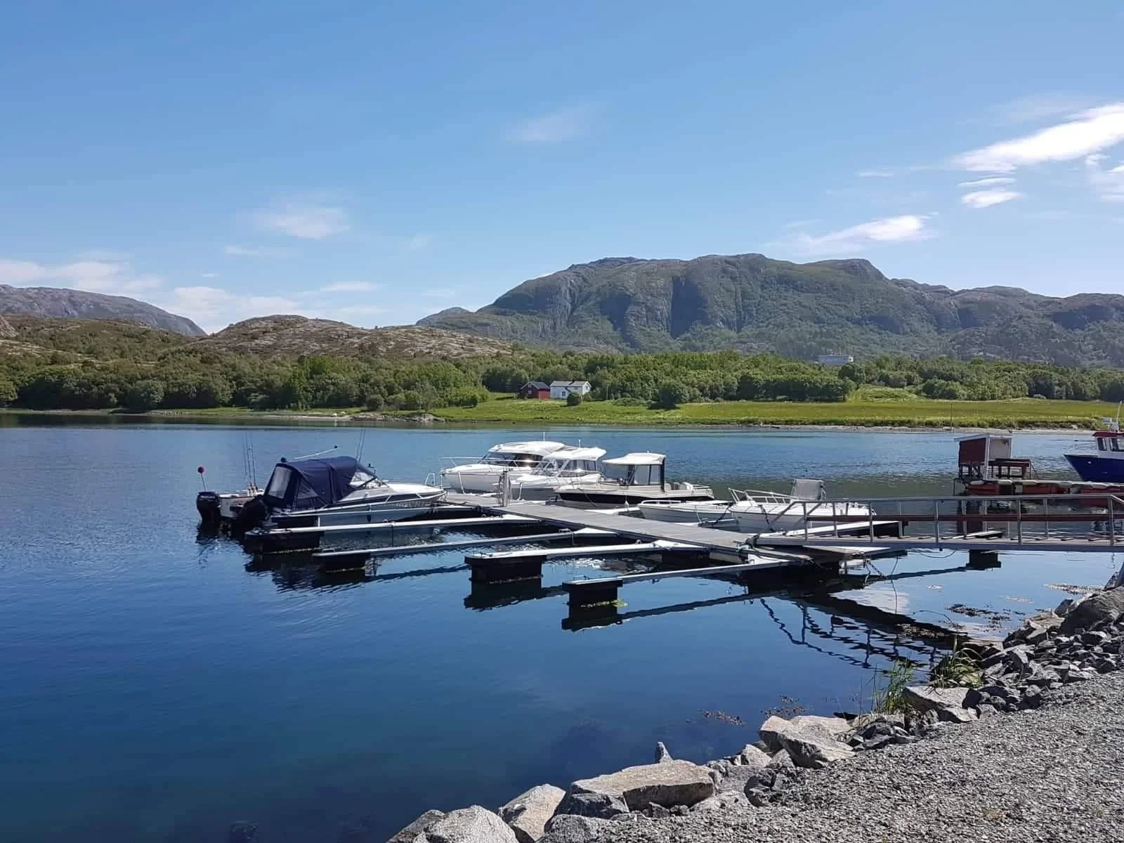 Blick auf einen kleinen Hafen mit mehreren Motorbooten und Yachten, umgeben von Bergen und grünen Hügeln bei sonnigem Wetter.