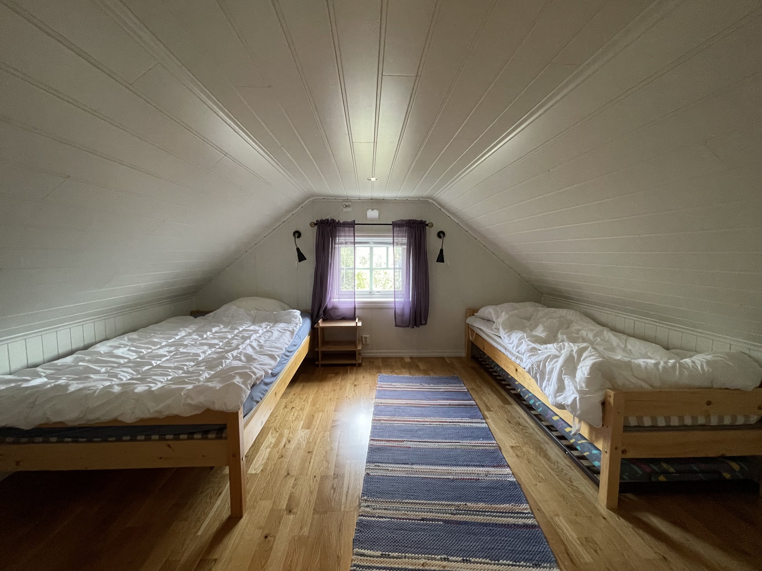 Ein Schlafzimmer mit zwei Einzelbetten, einem Fenster mit violetten Vorhängen und einem Holzboden.
