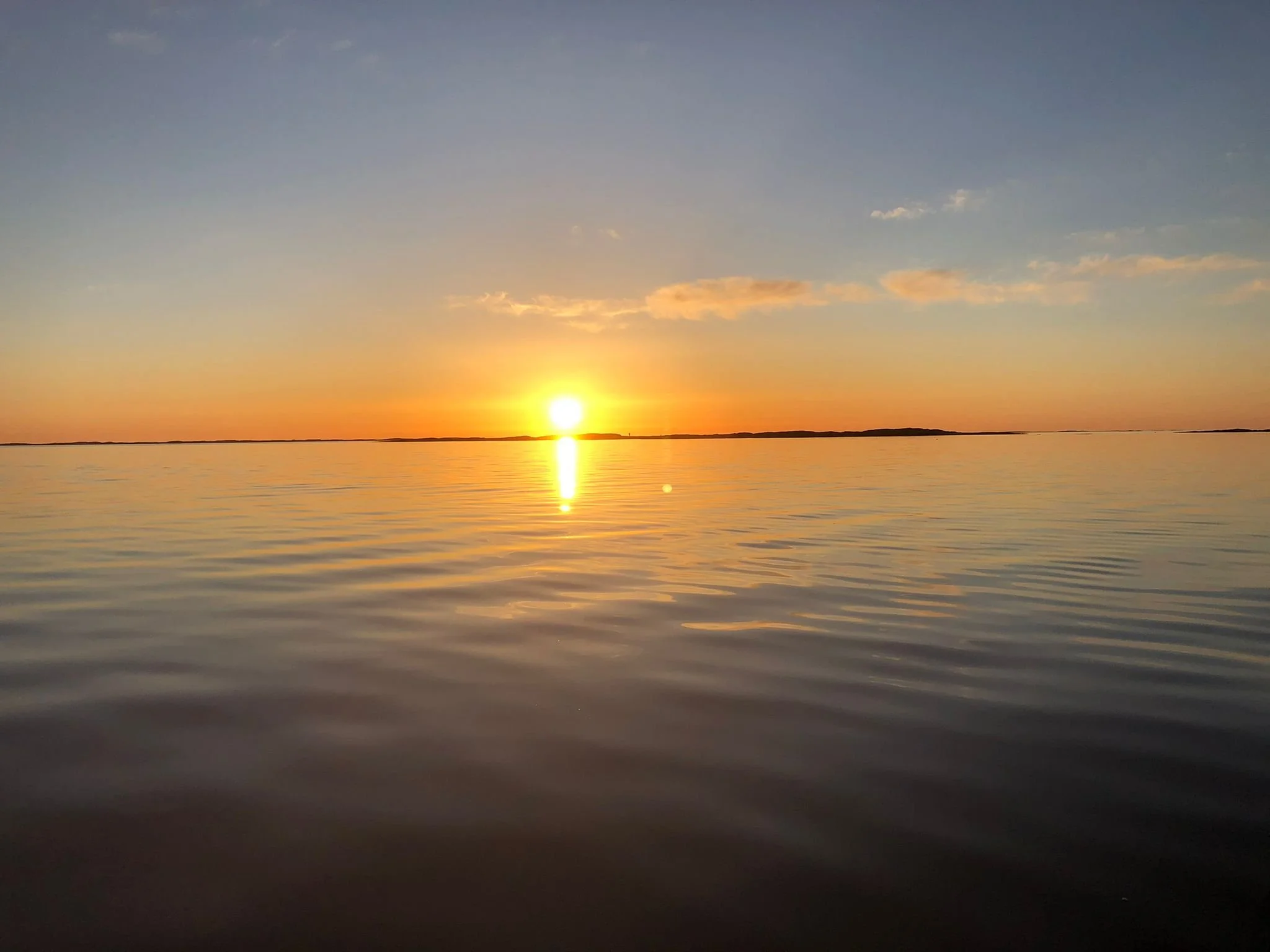 Sonnenuntergang über einem ruhigen See, mit reflektierendem Wasser und wenigen Wolken am Himmel.