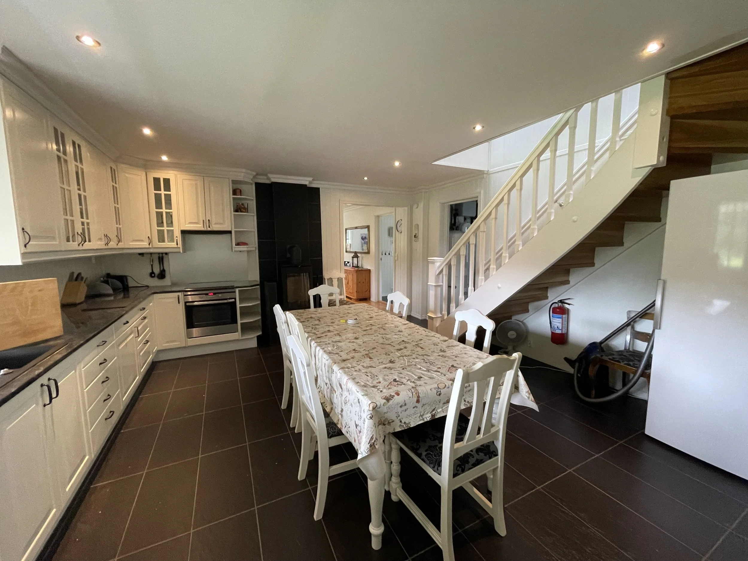Innenaufnahme einer Küche mit Esstisch, weißen Stühlen, weißen Küchenschränken und Holztreppe.