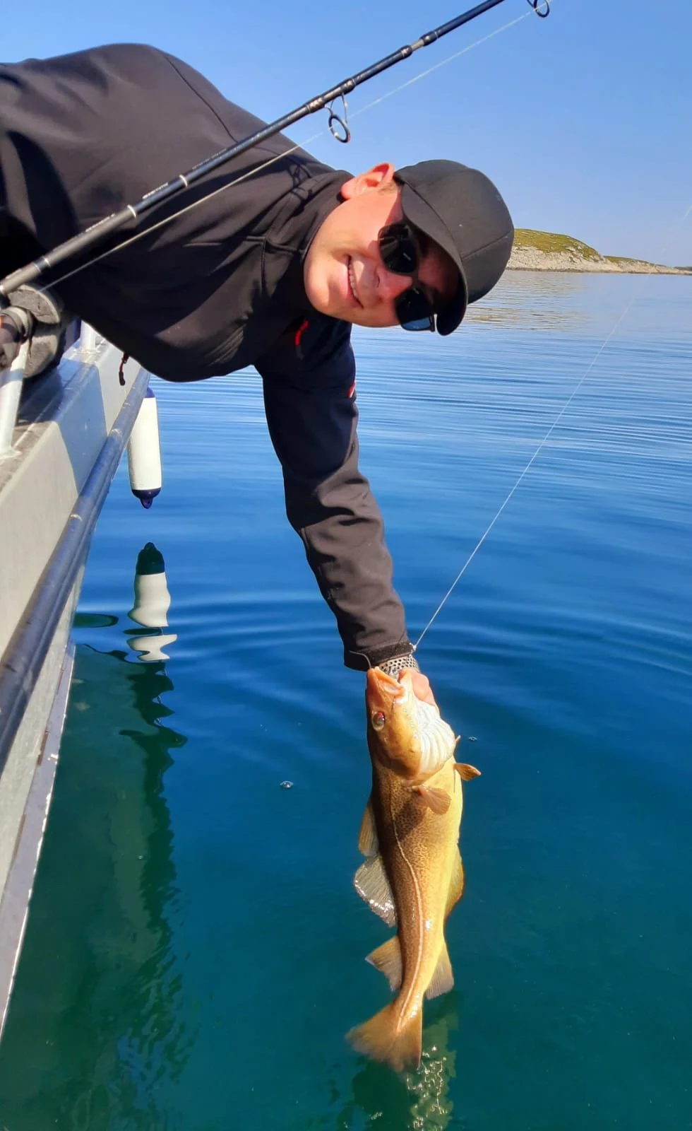 Mann im Schlafanzug hält einen großen Fisch beim Angeln auf einem Boot in ruhigem Wasser bei sonnigem Himmel.
