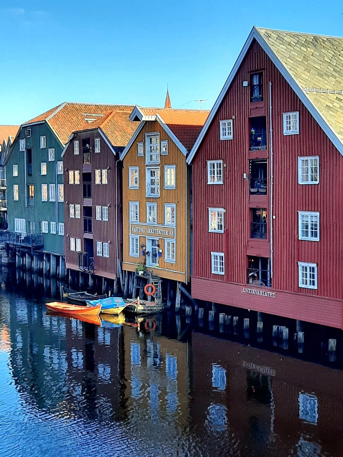 Bunte Holzhäuser am Wasser in Bergen, Norwegen, mit kleinen Booten im Wasser, klare blauer Himmel.