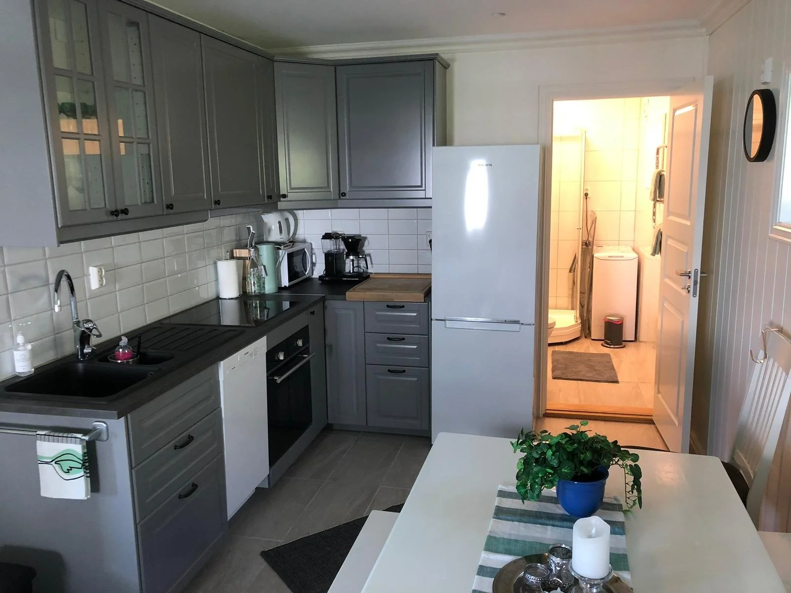 Küche mit grauen Schränken, Herd, Kühlschrank, Küchenutensilien, Esstisch mit grüner Pflanze