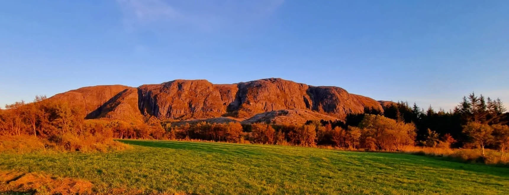 Eine Bergkette bei Sonnenuntergang mit einem grünen Feld im Vordergrund.