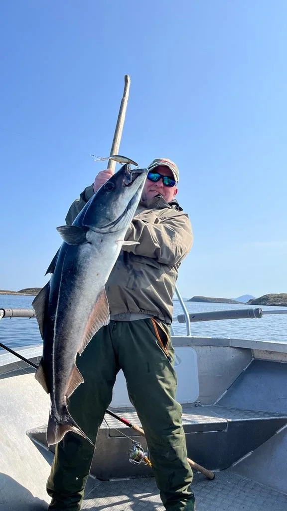 Ein angler zeigt stolz seinen großen Fisch auf einem Boot im Meer unter klarem Himmel.