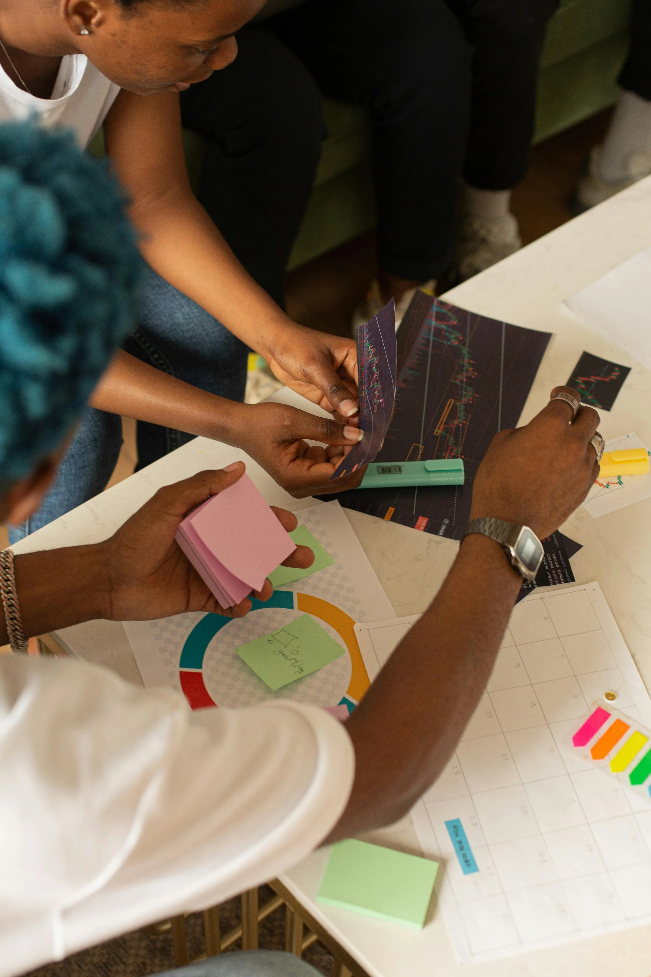 People gathered around a table reviewing charts, sticky notes, and colored markers, indicating a collaborative planning or brainstorming session.