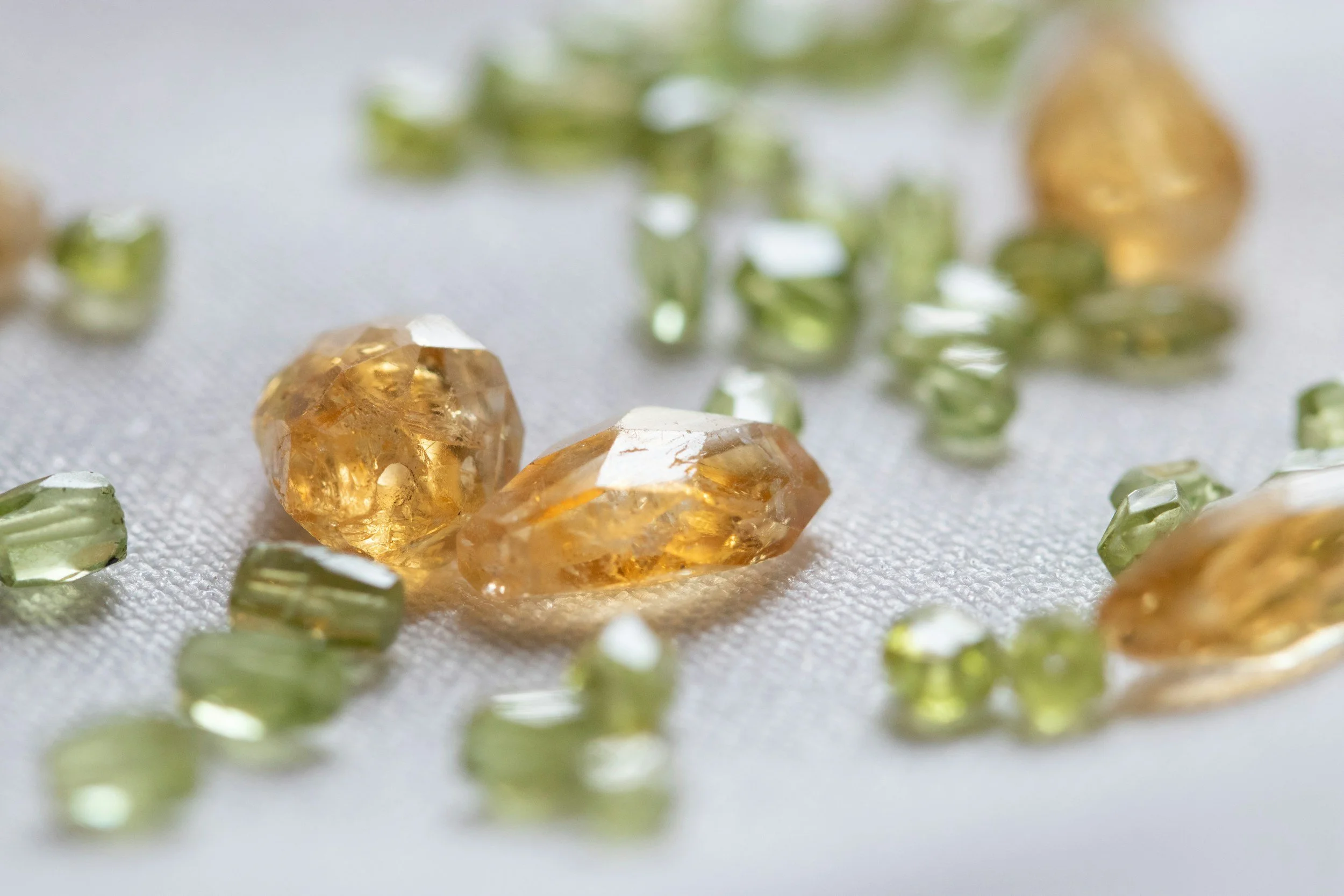 Various green and amber stones on a white cloth backdrop, of varying cut and clarity